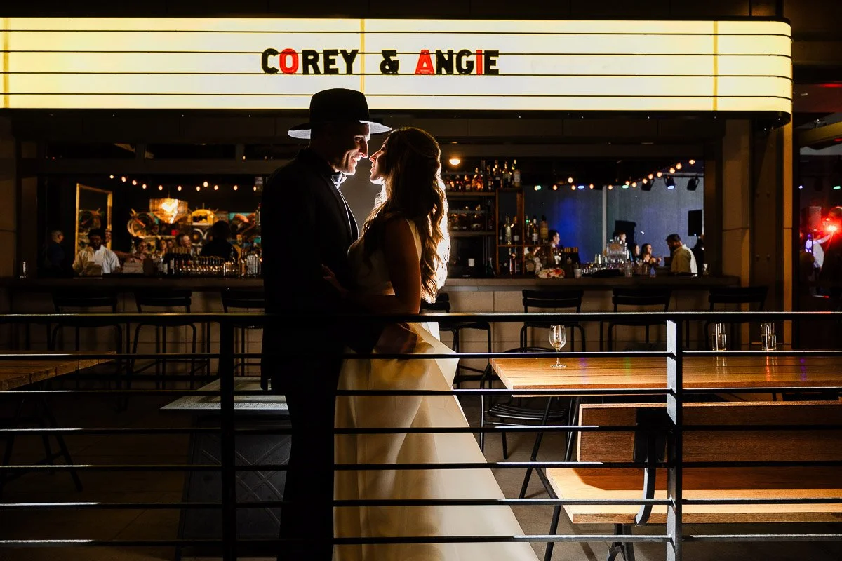 A couple stands embraced in silhouette against a warmly lit Magic Rat bar backdrop. A glowing sign above reads "Corey & Angie," adding a romantic touch during an Elizabeth Hotel wedding.