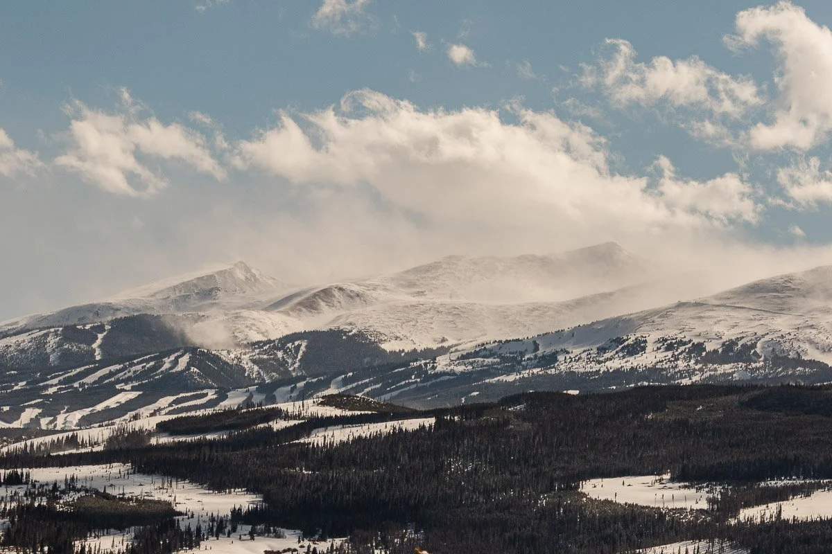 Snow-covered mountains under a blue sky with wispy clouds. The ski slopes carved into the terrain suggest a serene, winter recreational area.