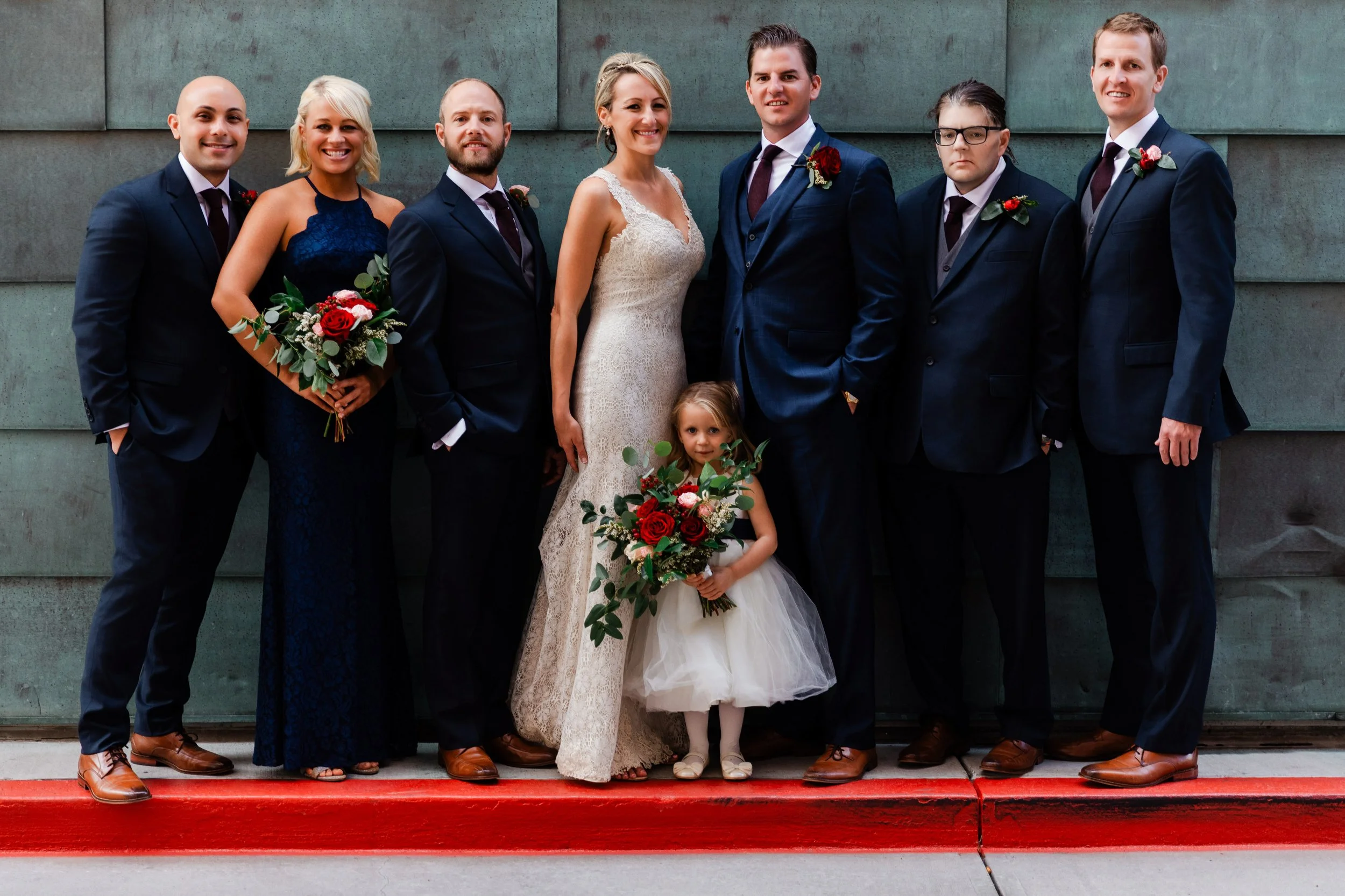Wedding party with bridesmaids, groomsmen and a flower girl pose for a formal photo on the city streets during Coohills Restaurant wedding reception in Denver, Colorado