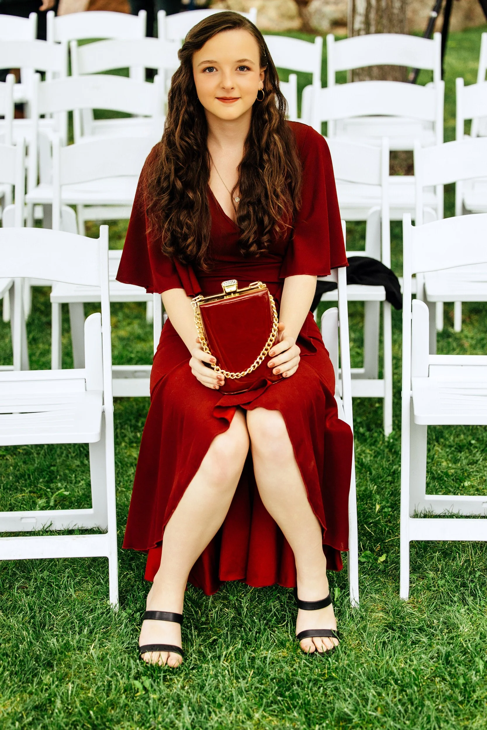 Woman with long hair in a red dress sits in white chairs awaiting a wedding ceremony at Greenbriar Inn in Boulder, Colorado