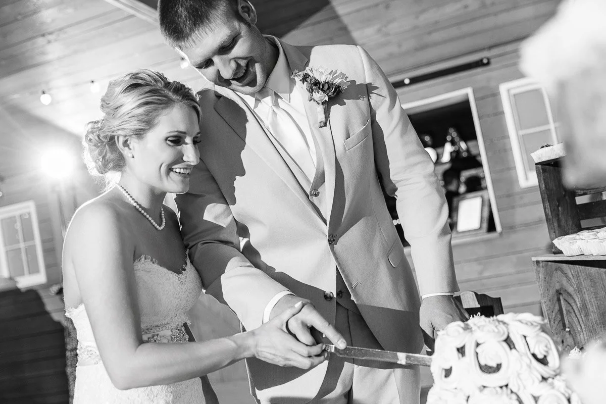 A joyful bride and groom in a wood-paneled venue cut a tiered wedding cake together, highlighting their happiness and love on their special day.
