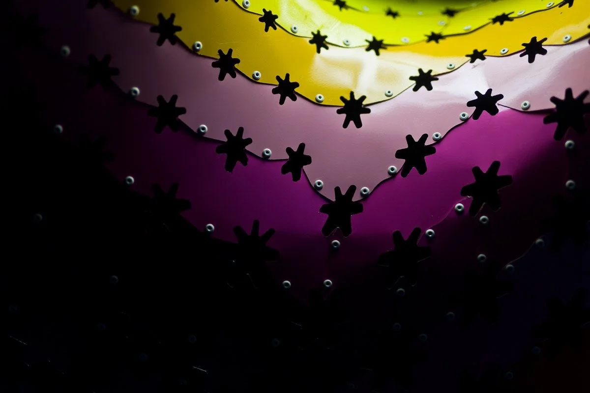 Abstract image featuring layered wavy patterns in yellow, orange, and pink gradients, overlaid with black star shapes, creating a vibrant, dynamic effect.