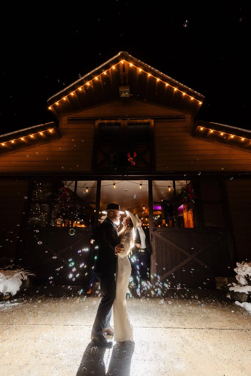 A couple embraces under glowing barn lights at night, surrounded by floating bubbles captured by La Joya Dulce wedding photographer tomKphoto