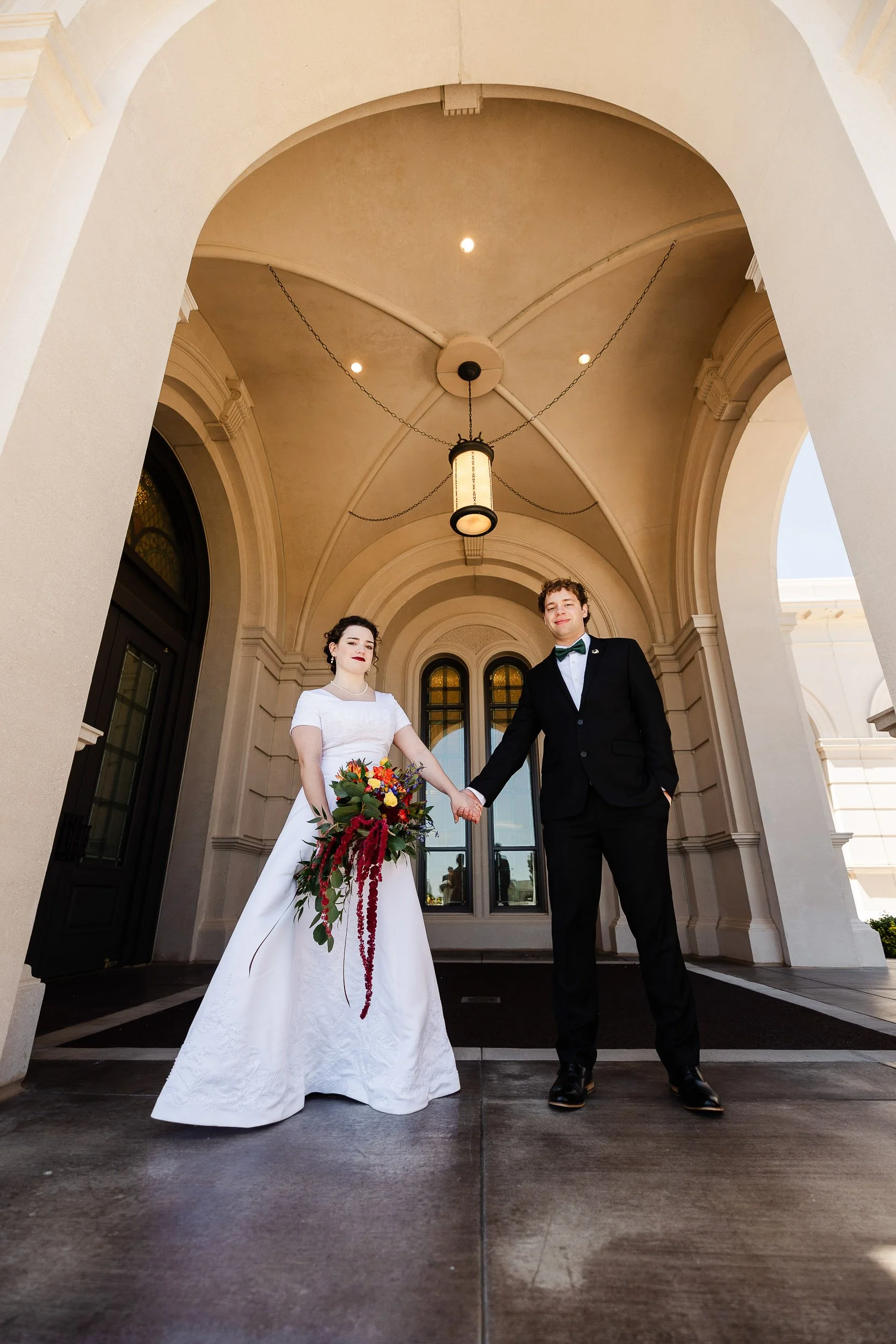 Vertical composition of bride and groom holding hands under the portico after a wedding at the LDS Temple in Fort Collins, Colorado