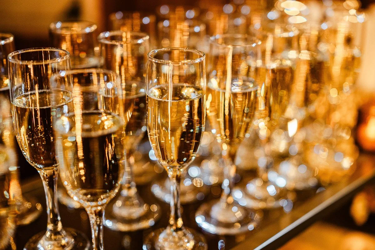 Rows of filled champagne flutes on a reflective surface, creating a festive and elegant atmosphere with warm, golden lighting.