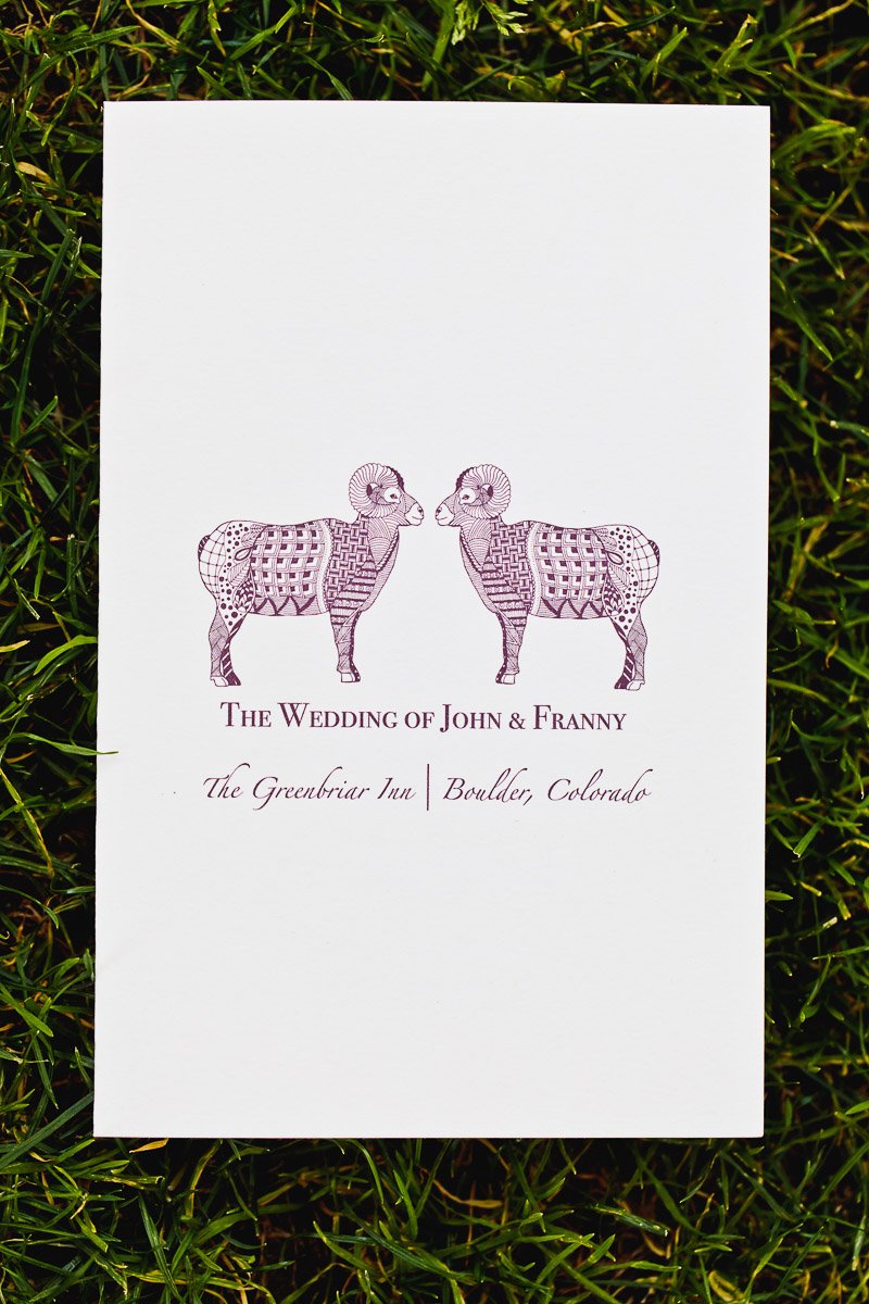 A wedding invitation card on grass features two intricately drawn purple sheep facing each other. Below, text reads "The Wedding of John & Franny" with venue details.