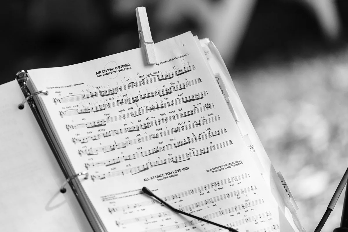 Black and white image of a music sheet in a binder, clipped open. Notes and lyrics are visible, creating a serene and focused atmosphere.