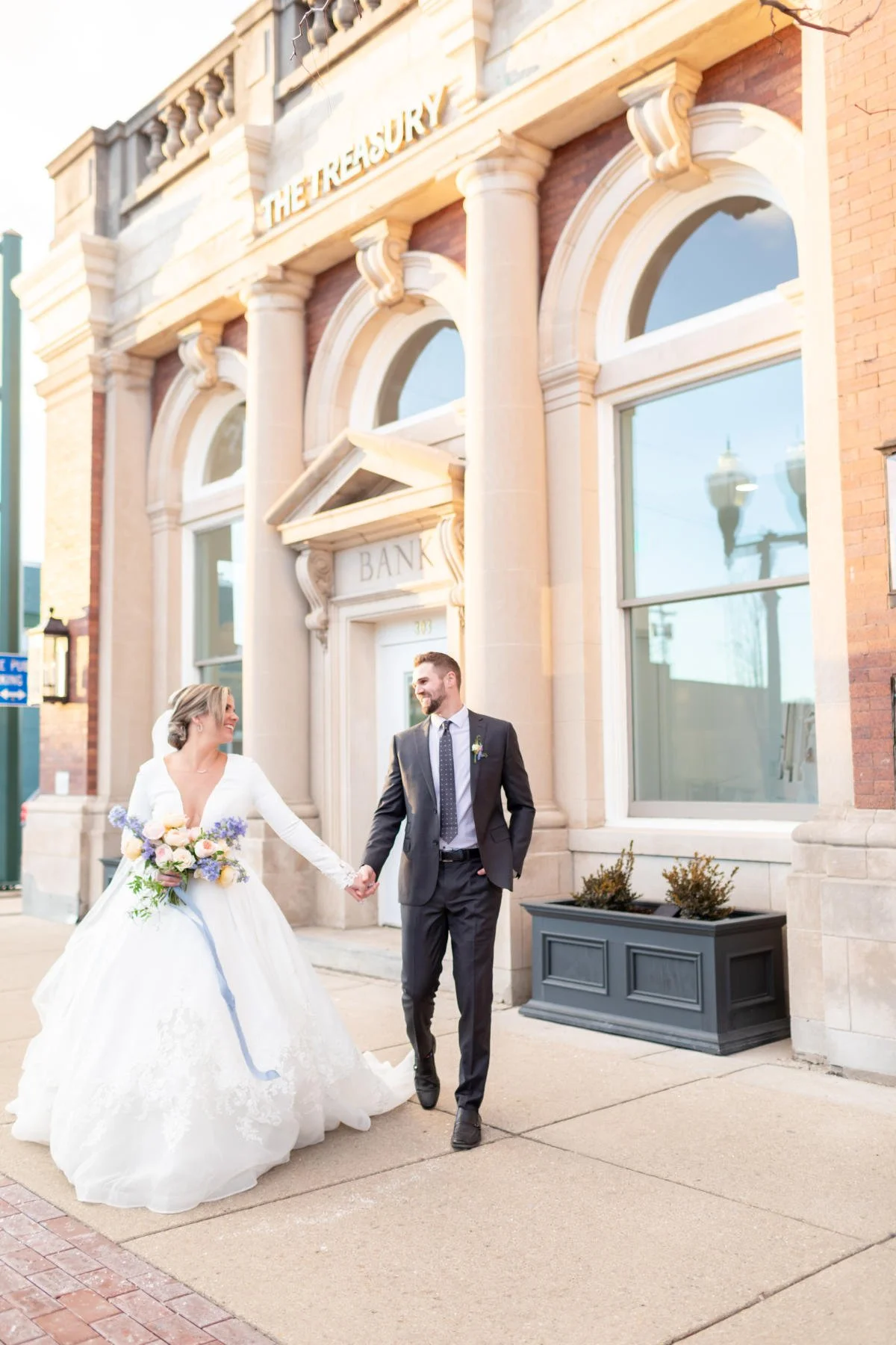 Bride and groom walking outside The Treasury wedding venue in Delavan Wisconsin in front of the historic bank building near Lake Geneva.