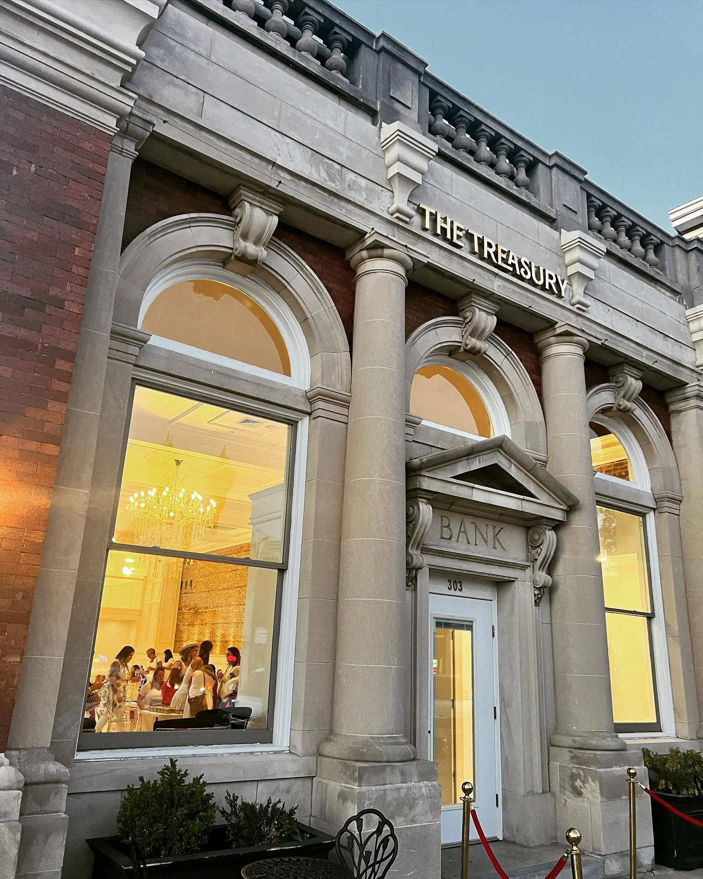 Exterior of The Treasury historic wedding venue in Delavan Wisconsin with large arched windows and chandeliers visible inside the reception space.
