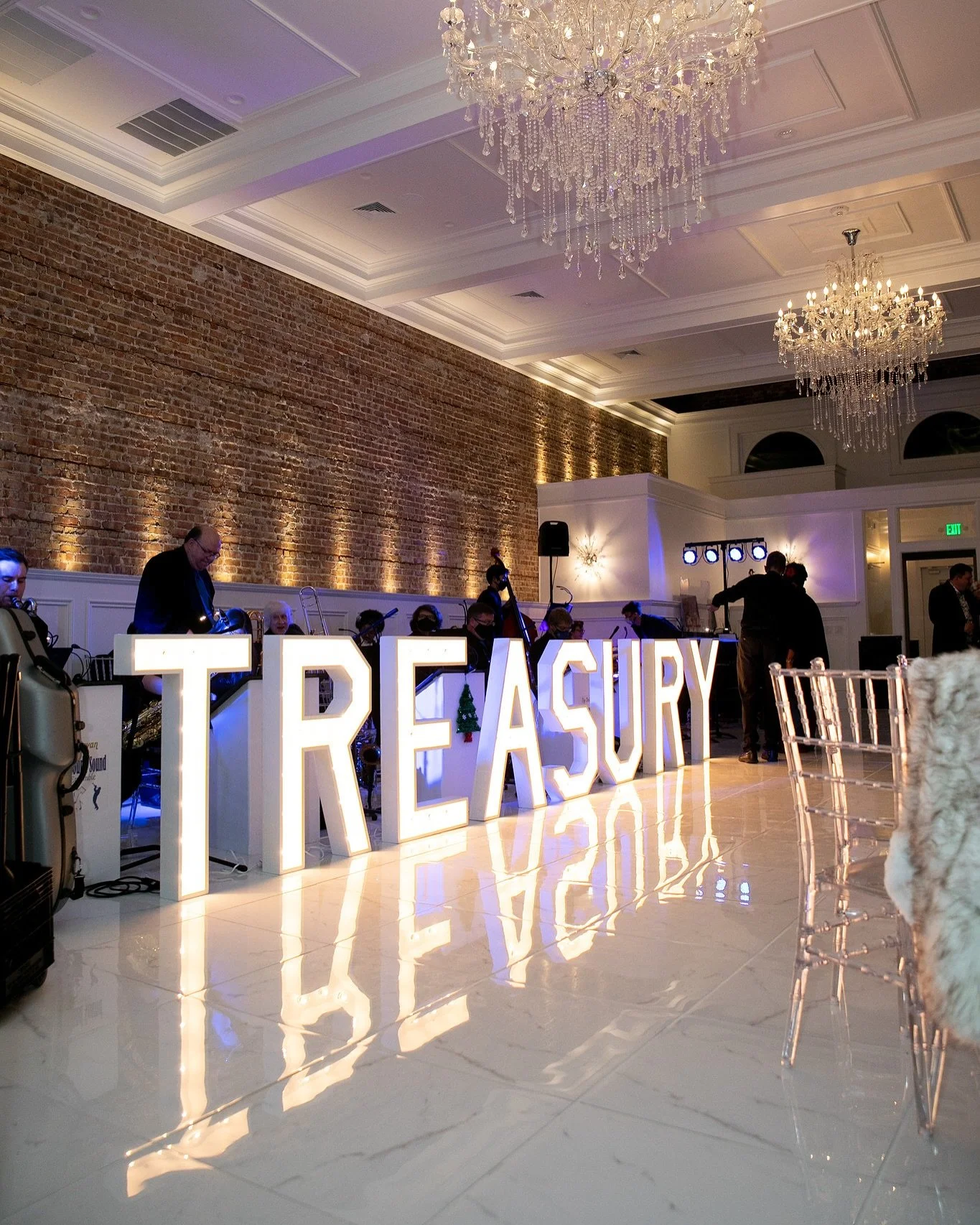 Wedding reception at The Treasury venue in Delavan Wisconsin featuring chandeliers, exposed brick walls, and illuminated venue signage.
