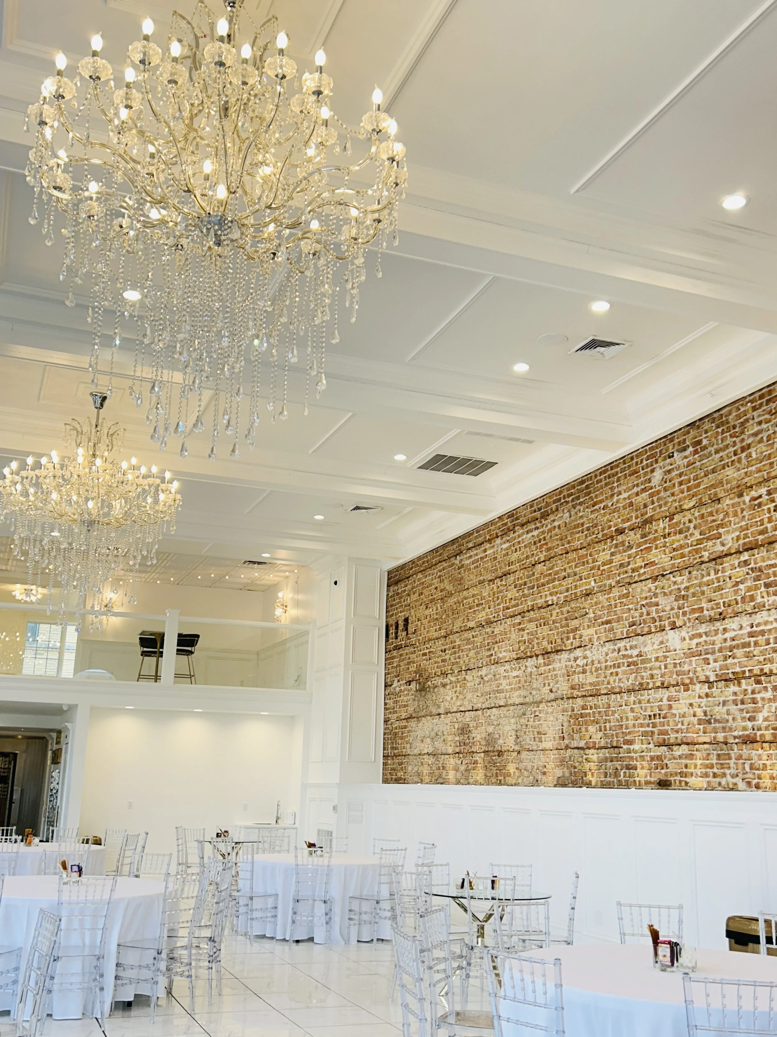 Elegant interior of The Treasury wedding venue in Delavan Wisconsin featuring crystal chandeliers, exposed brick wall, and bright white reception space.