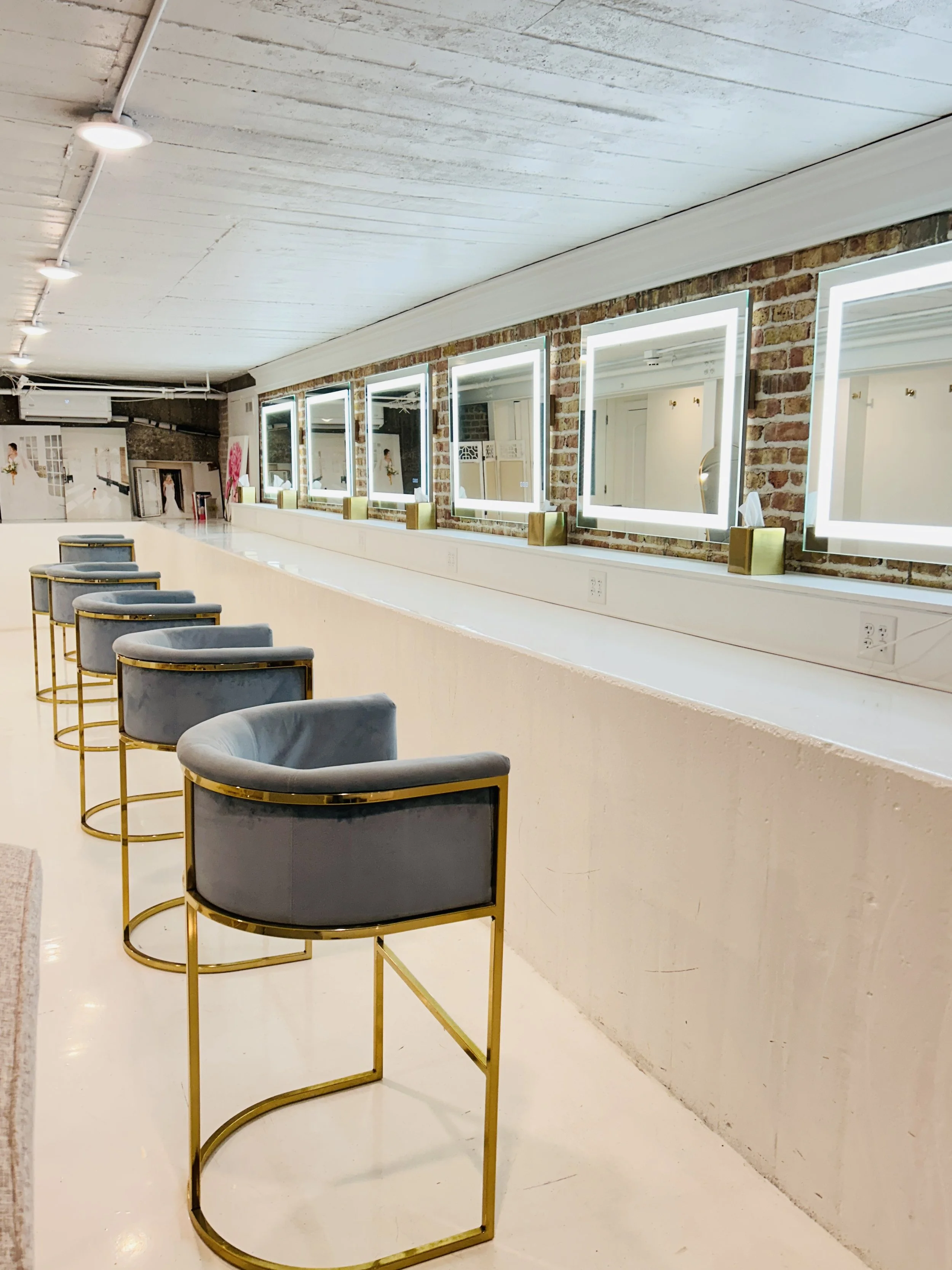 Bridal getting ready area at The Treasury wedding venue in Delavan Wisconsin featuring lighted vanity mirrors, exposed brick wall, and velvet bar stools.