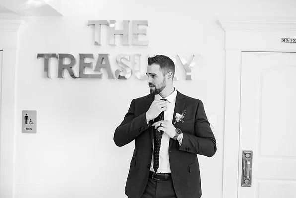 Groom adjusting his tie in front of The Treasury wedding venue sign in Delavan Wisconsin.