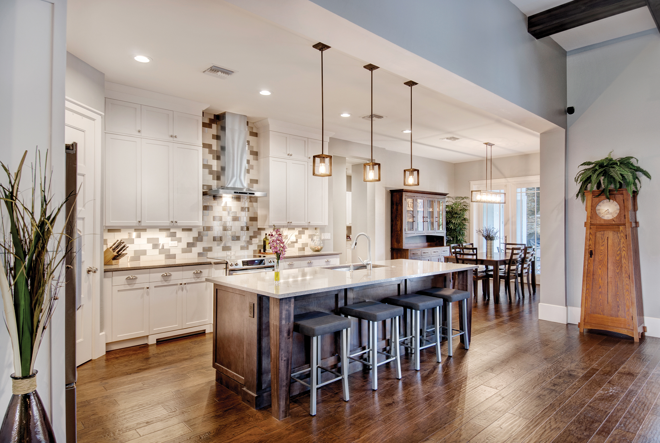  The great room flows directly into the airy kitchen. Shaker-style cabinetry is set against a subway tile backsplash with metallic accent tiles. A modern stainless steel hood and Edison bulb lights are a perfect example of how modern and traditional 