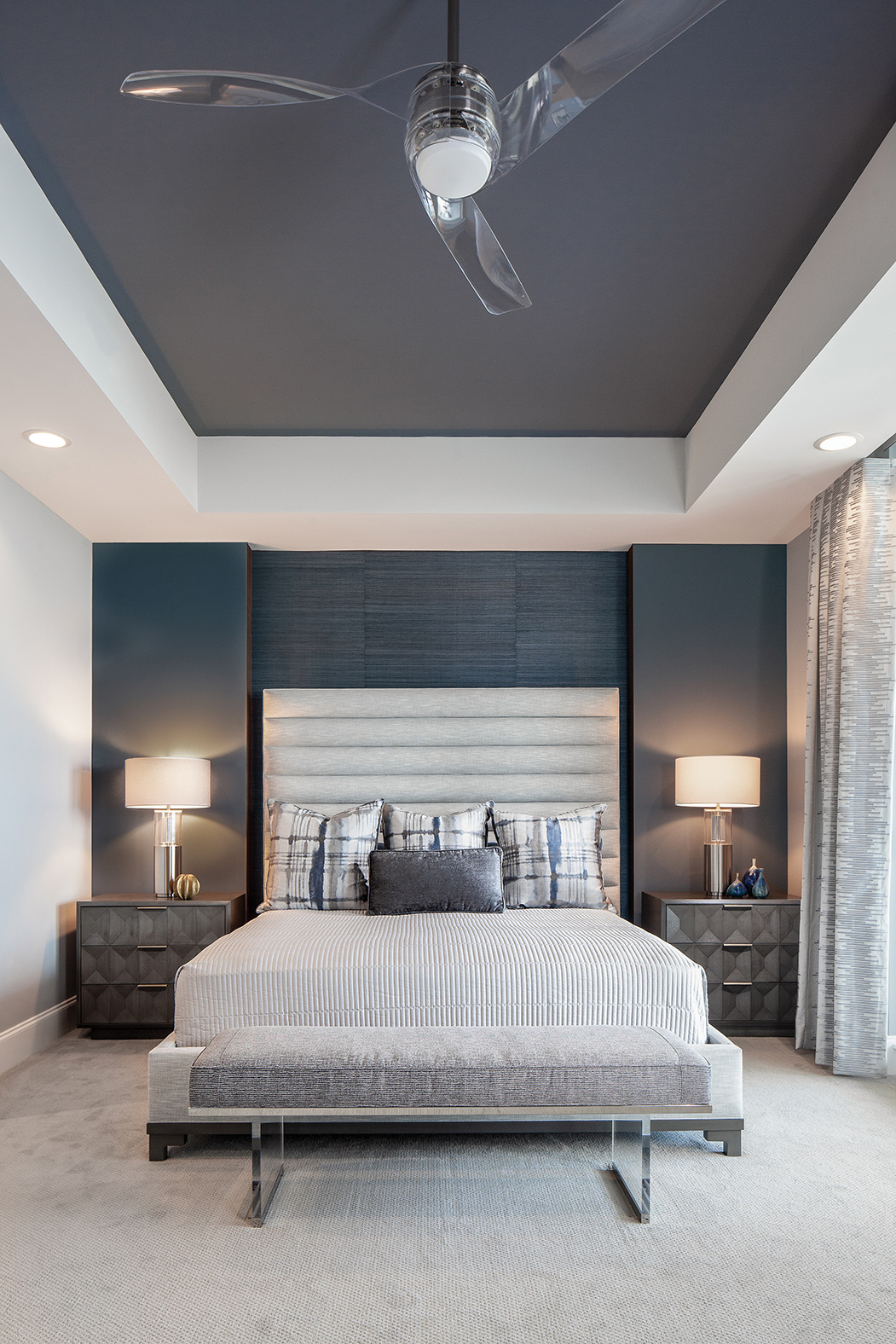  In the next unit, the deep blue walls and ceiling in the master bedroom provides a dramatic backdrop. “This room is interesting because it’s long and deep and the focal point is the back wall. We needed to add interest through depth and dimension, s