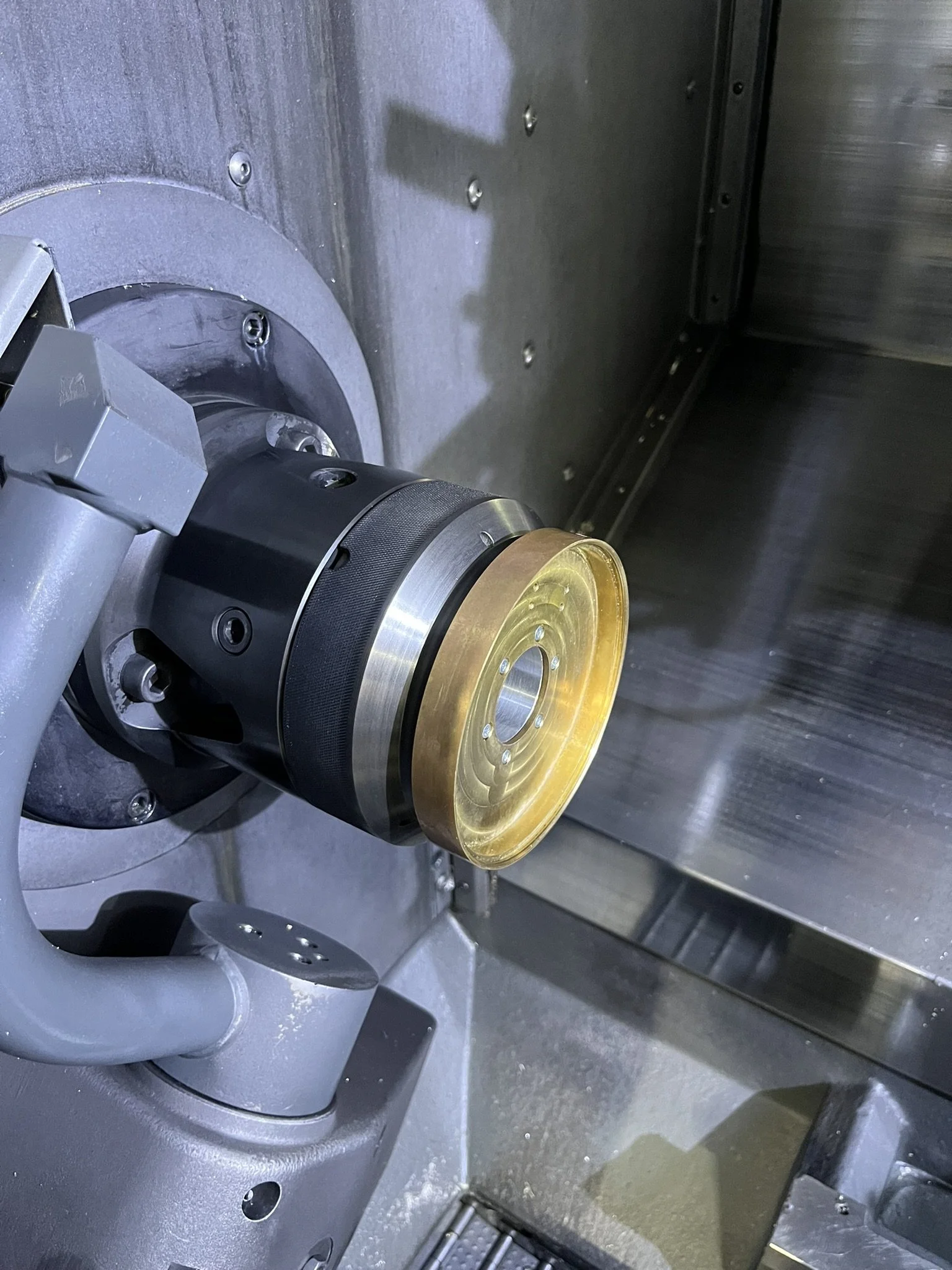 Large custom brass lighting canopy secured in a CNC lathe jig during machining, allowing accurate and repeatable production.