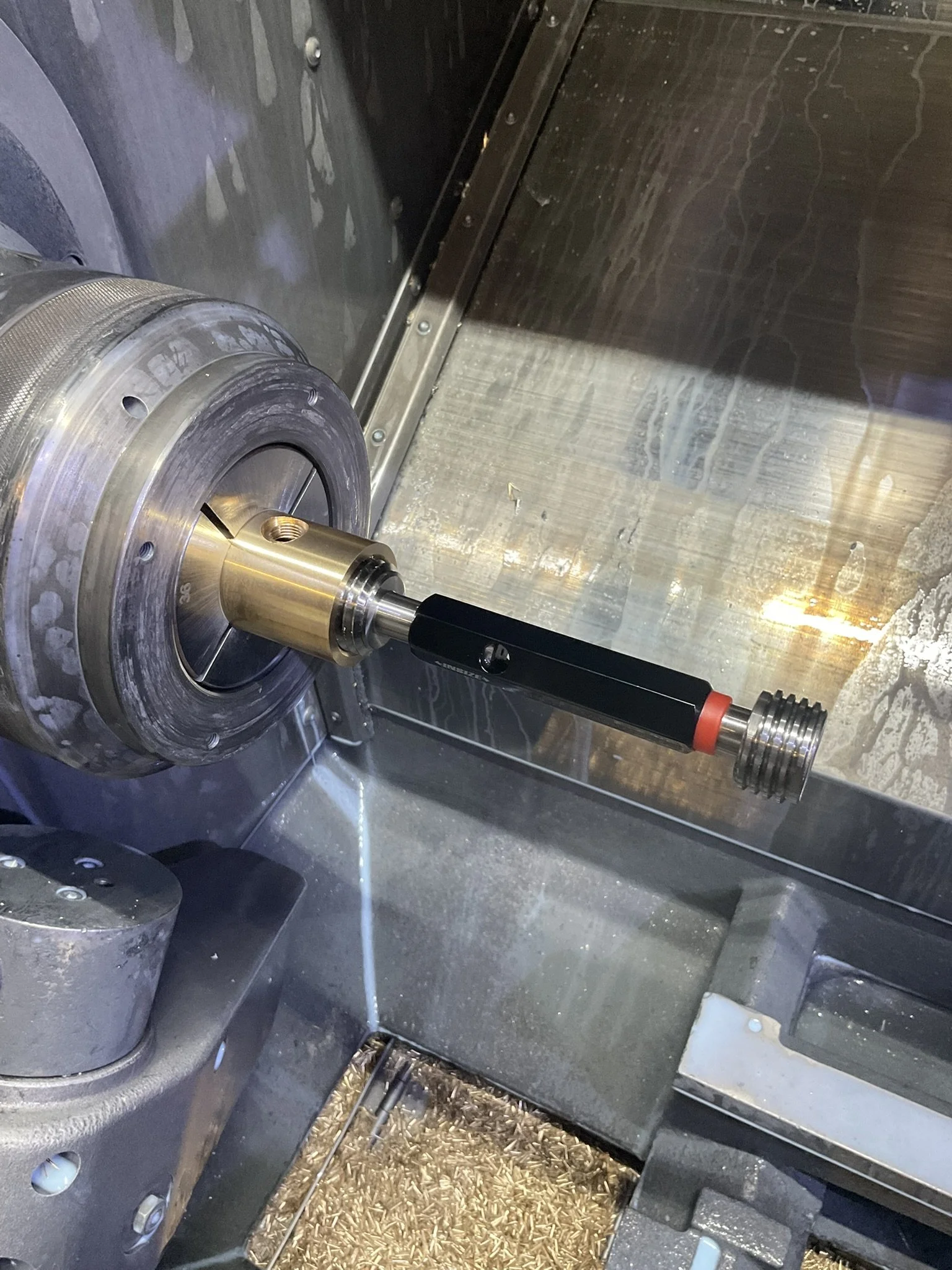 Brass component in the lathe with thread checked using a go/no-go gauge for fit and consistency.