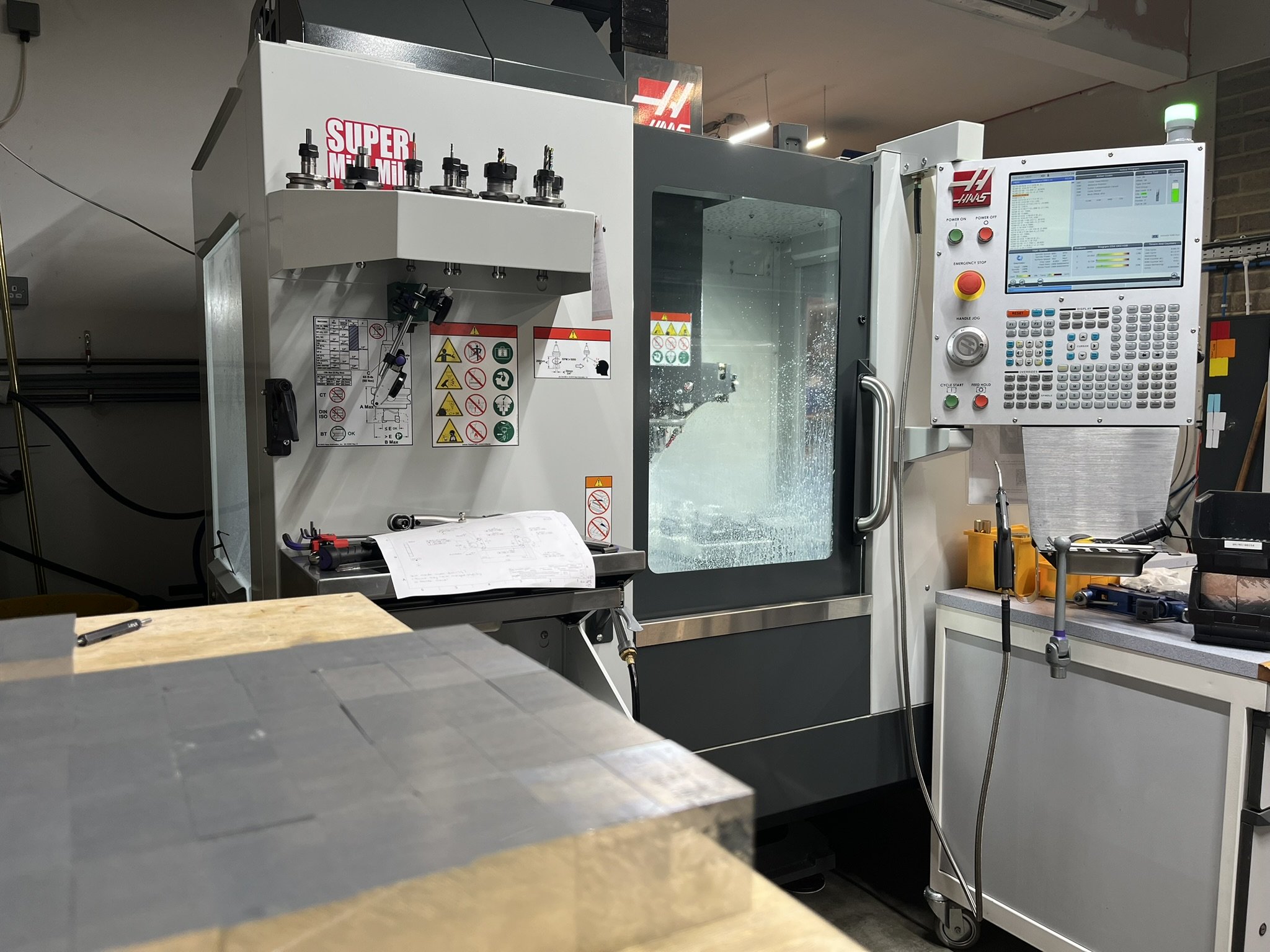Cut aluminium billets prepared for CNC milling on a workshop shelf beside the machine