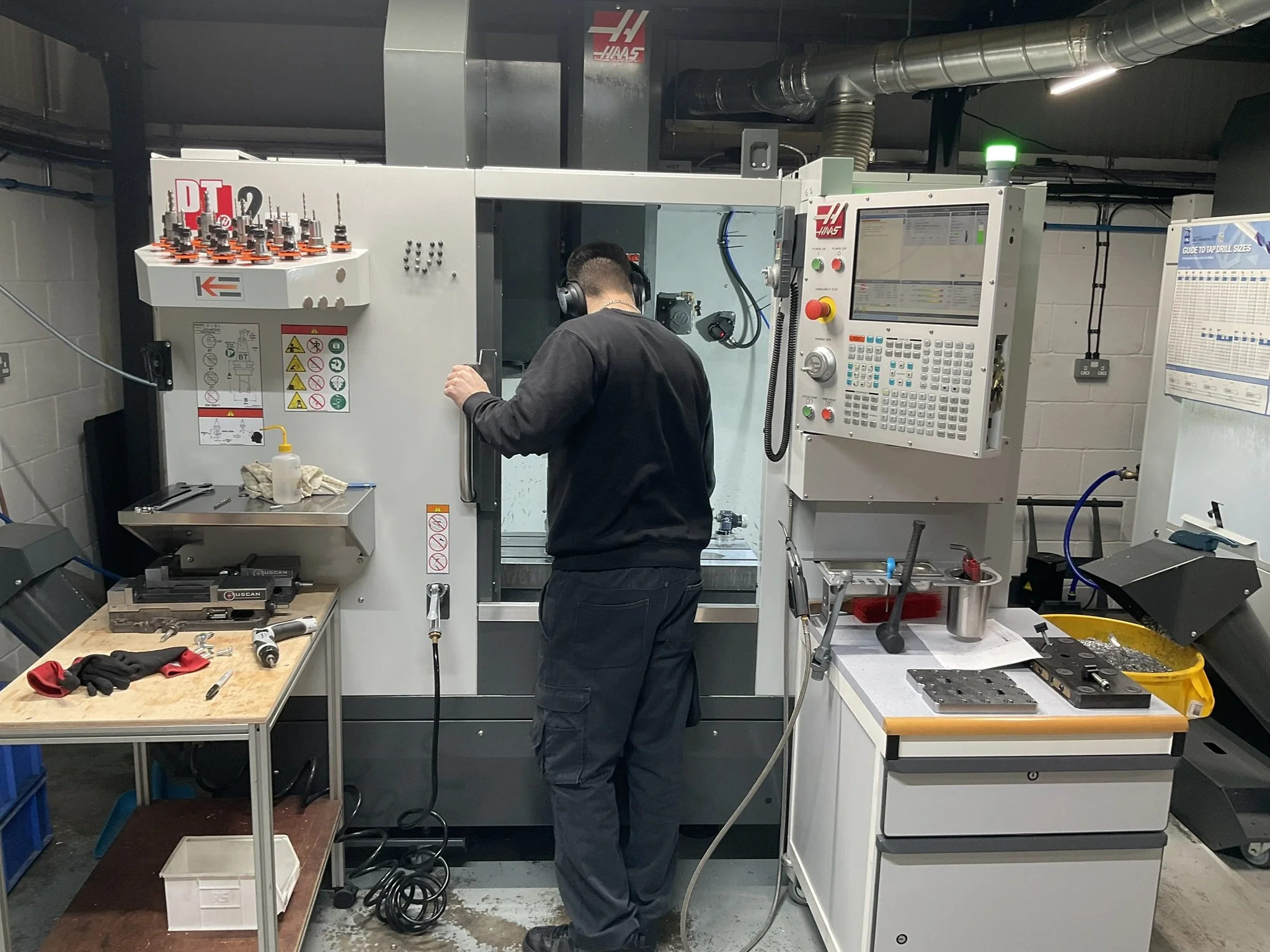 Engineer standing in front of a CNC milling machine with tooling and machined parts beside the setup.