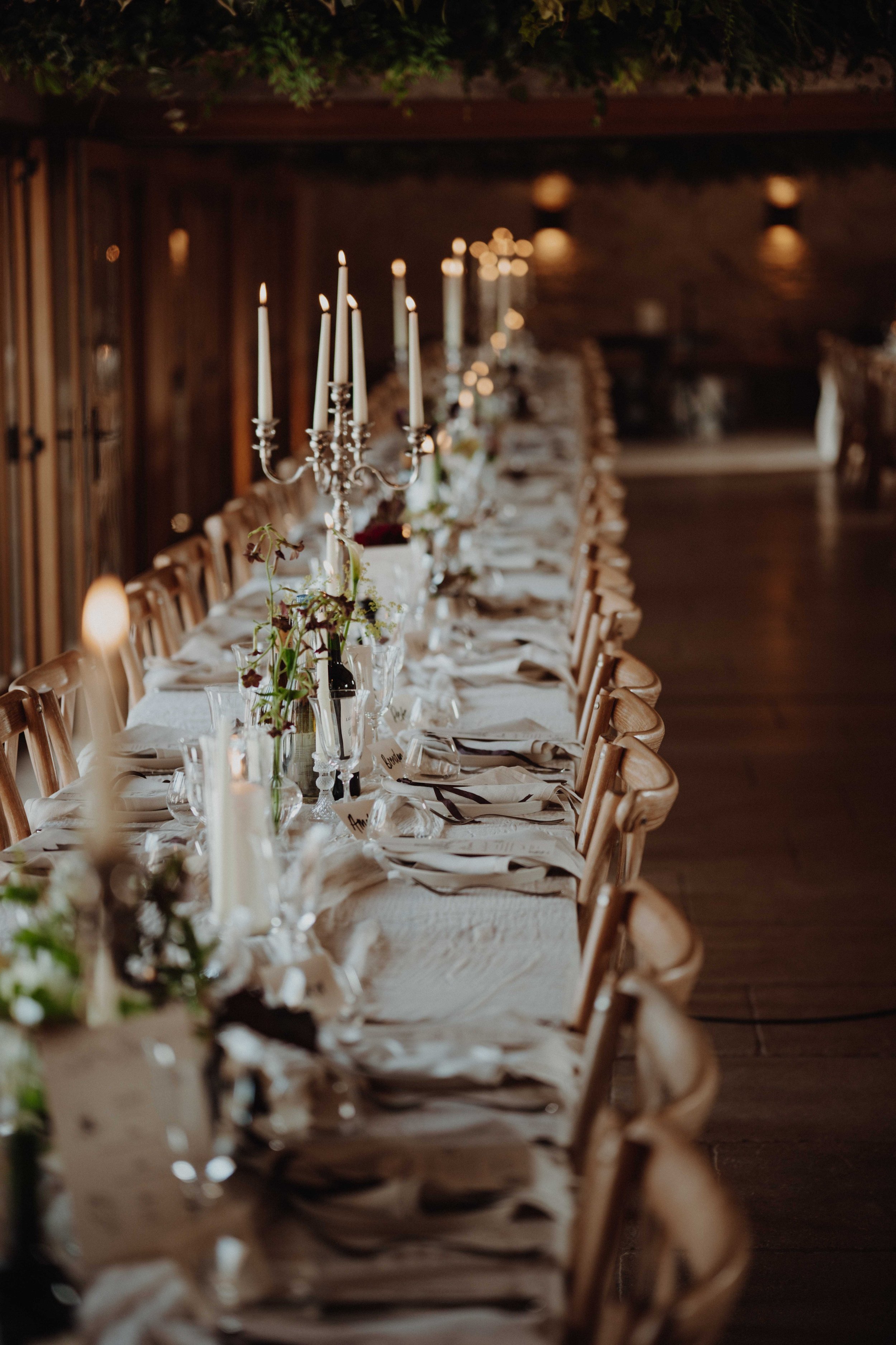 Elegant long banquet table set for a formal event with candles and floral centerpieces in a rustic wooden interior.