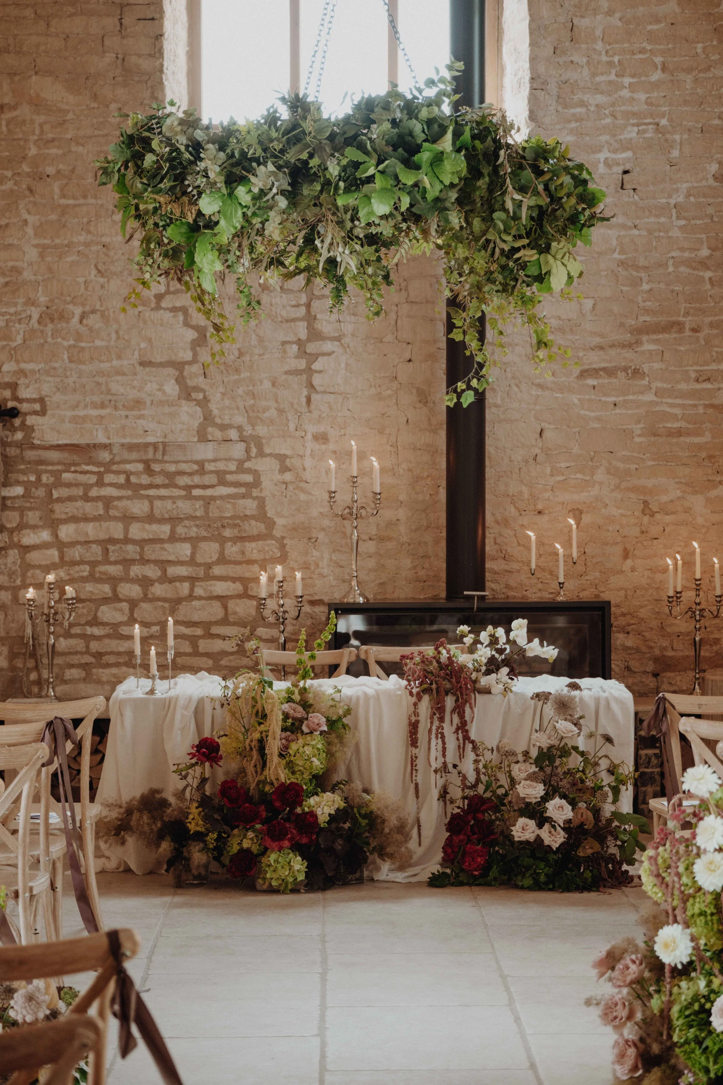Wedding or event decor with a brick wall, hanging greenery, floral arrangements, and candelabras.