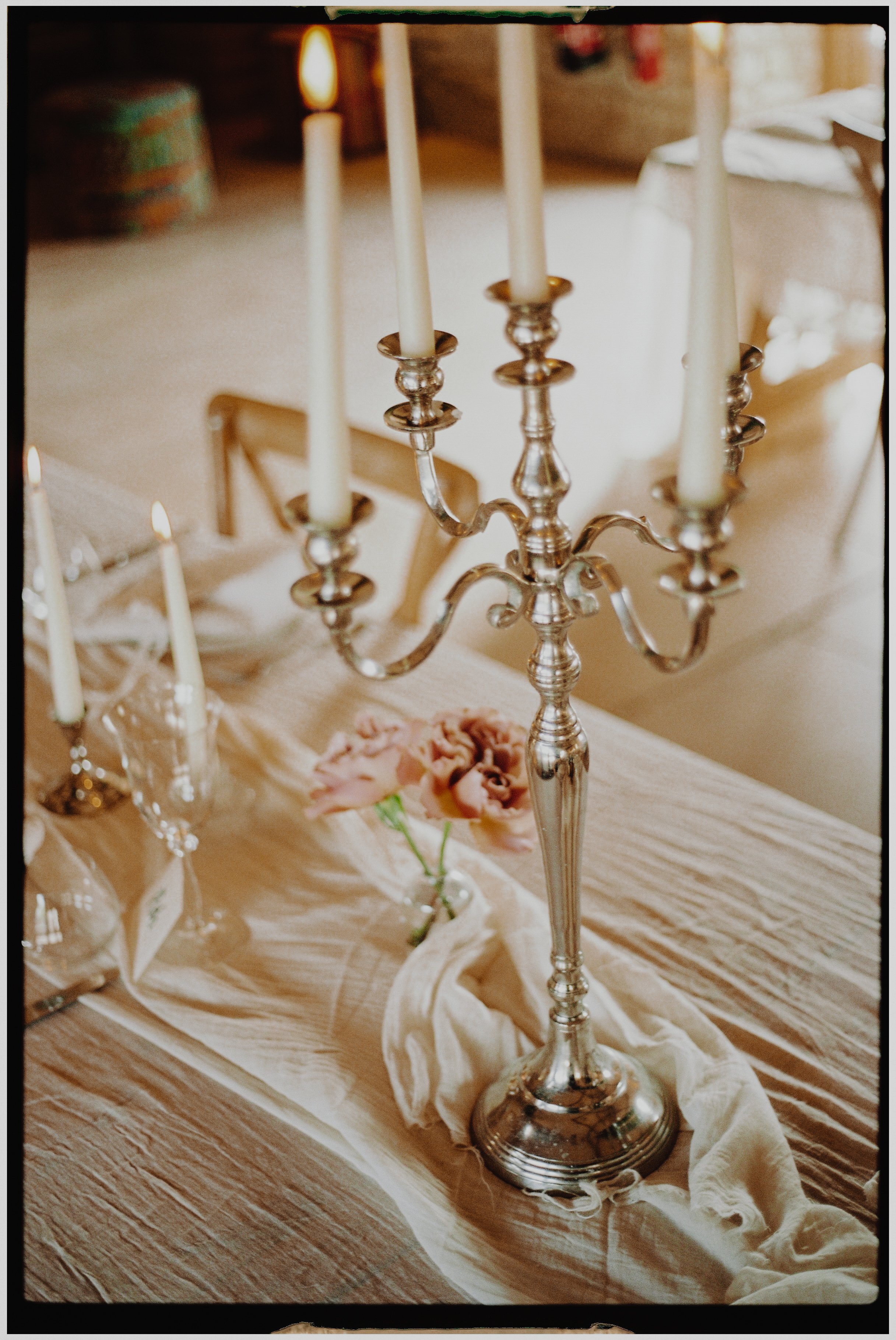 A silver candelabrum with five lit candles on a decorated table with a draped table runner and pink flowers.