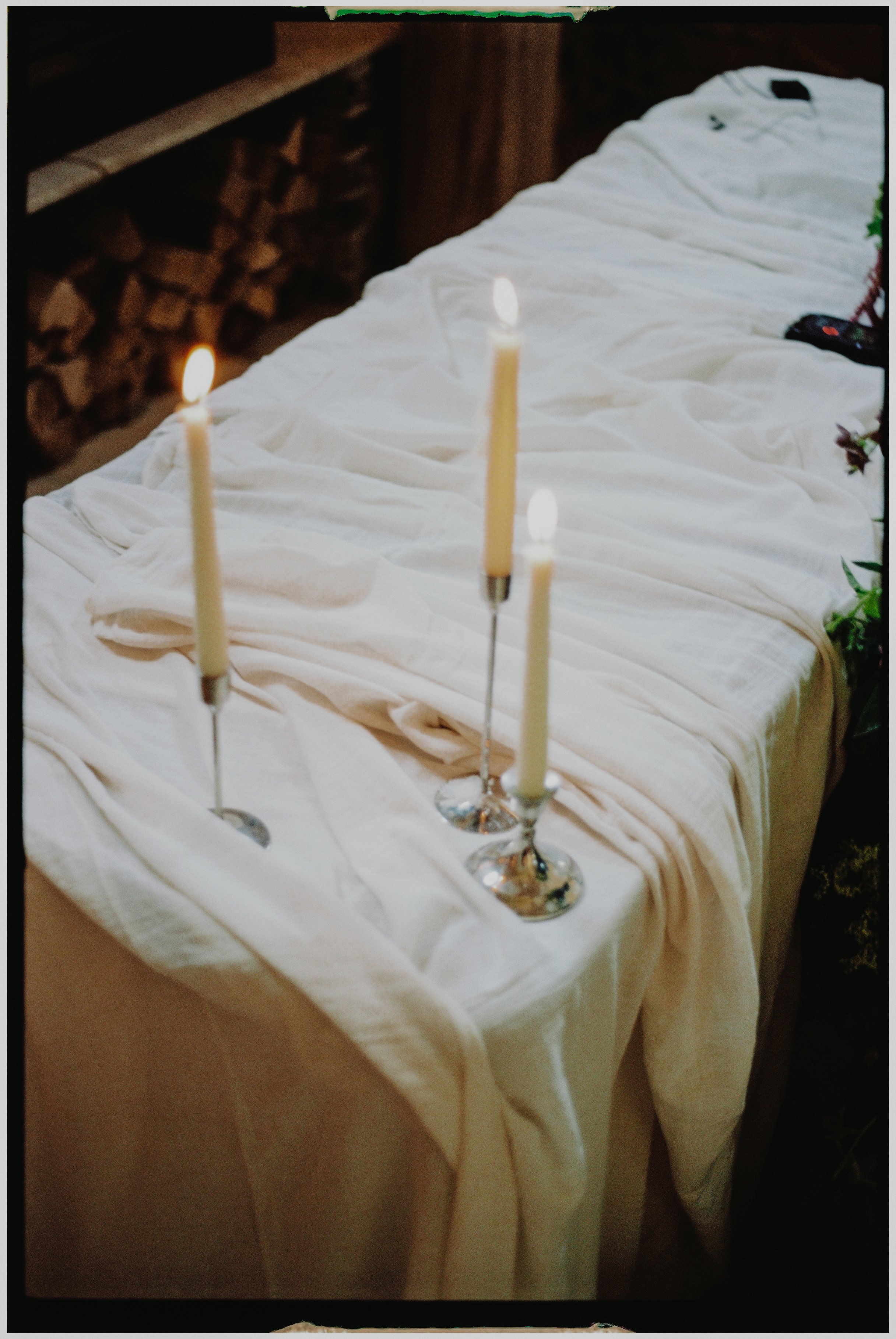 A table covered with white cloth, three lit candles in silver candlesticks, and some Christmas decorations on the side.