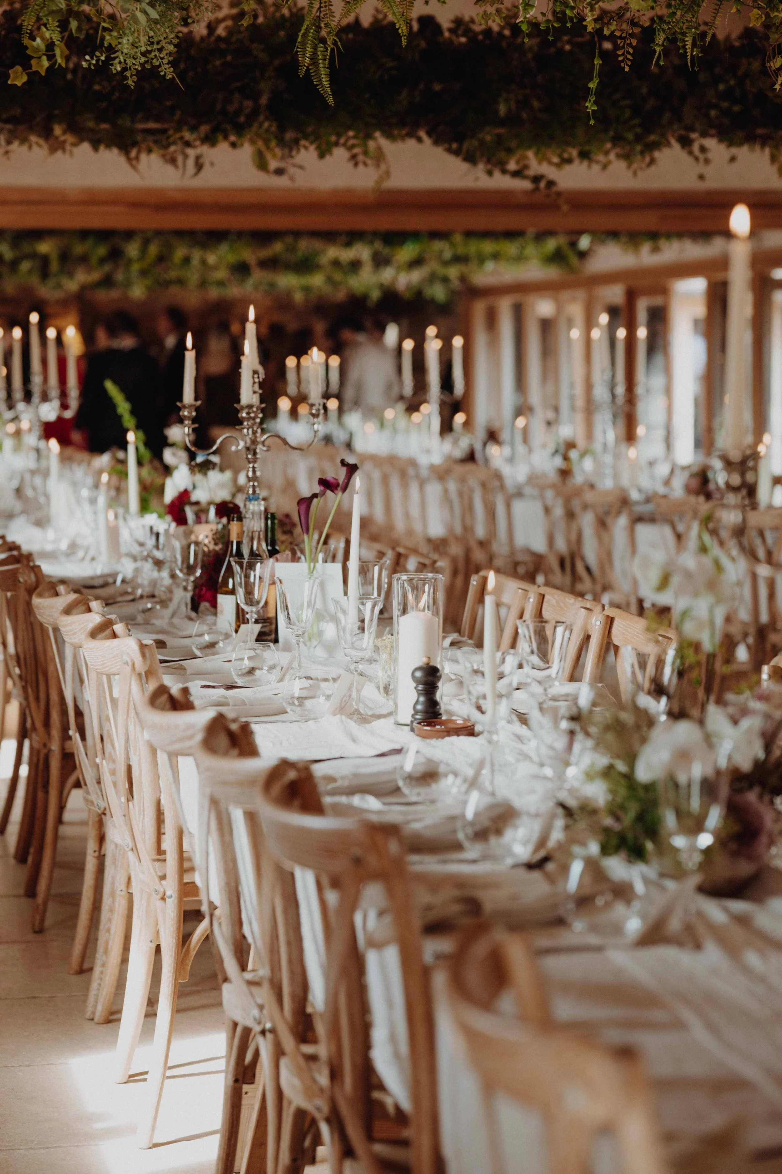 Decorated banquet table at an indoor event, with candles, flowers, glasses, and tableware.