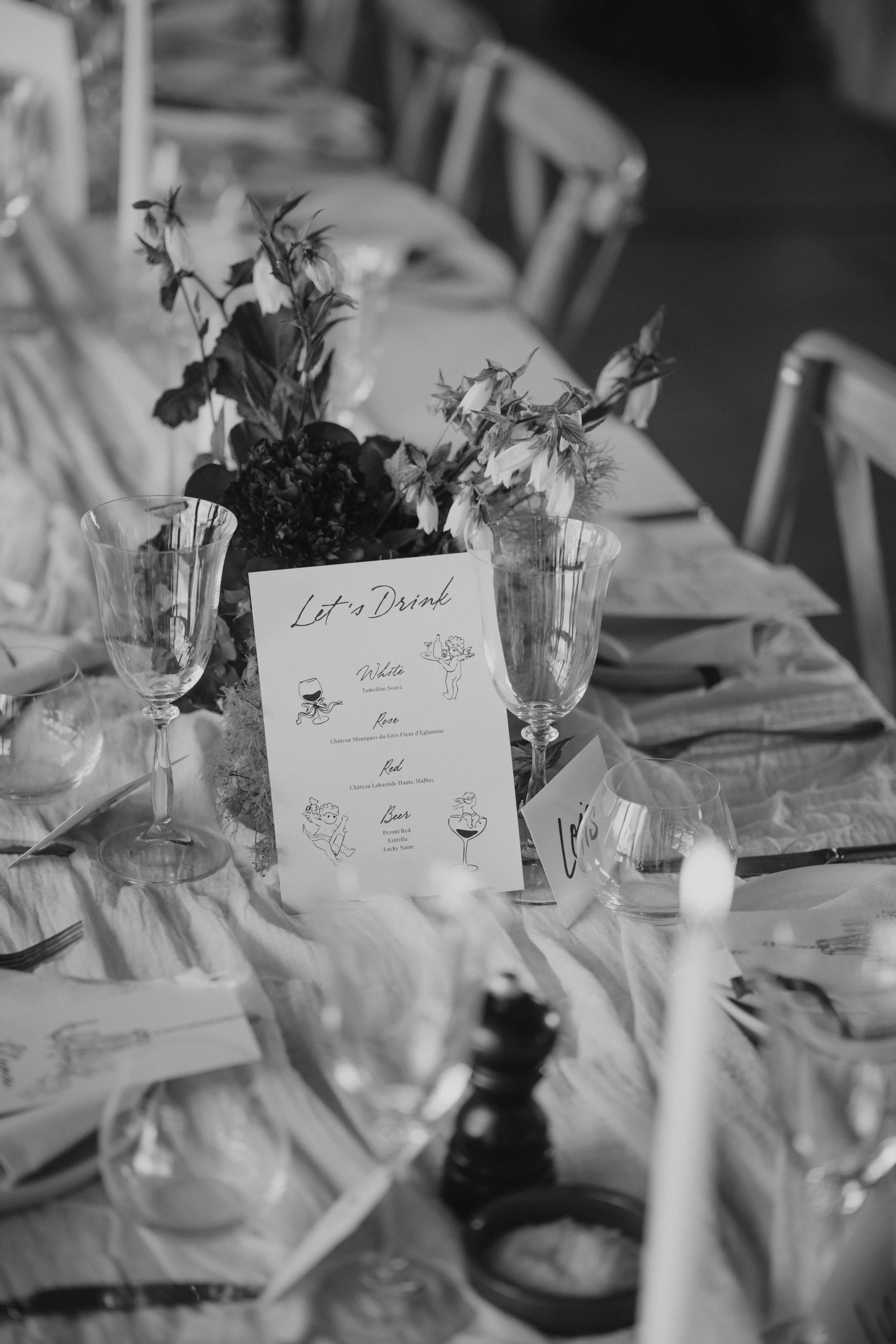 A close-up of a table setting at an event, featuring a floral centerpiece, wine glasses, a menu card, and lit candles