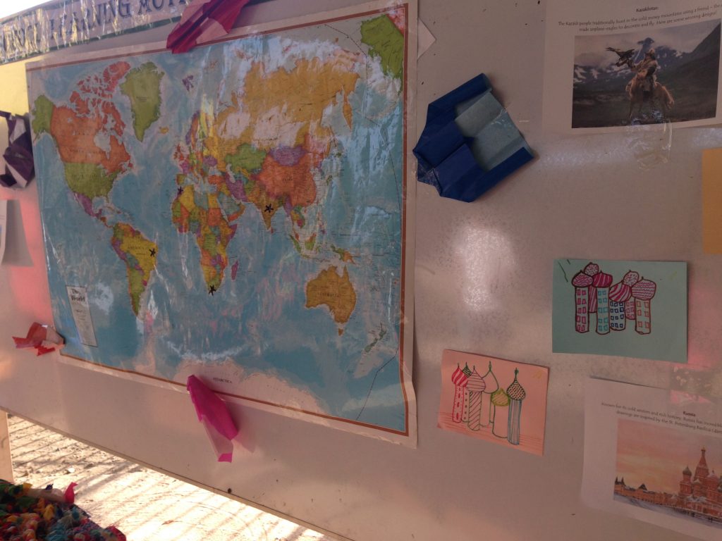   A map was the center of this board, filled with marks of the many places students traveled to this year. Around it, student art is displayed: St. Peter’s Basilica from Russia, and paper airplanes representing the companion hunting eagles from Kazak