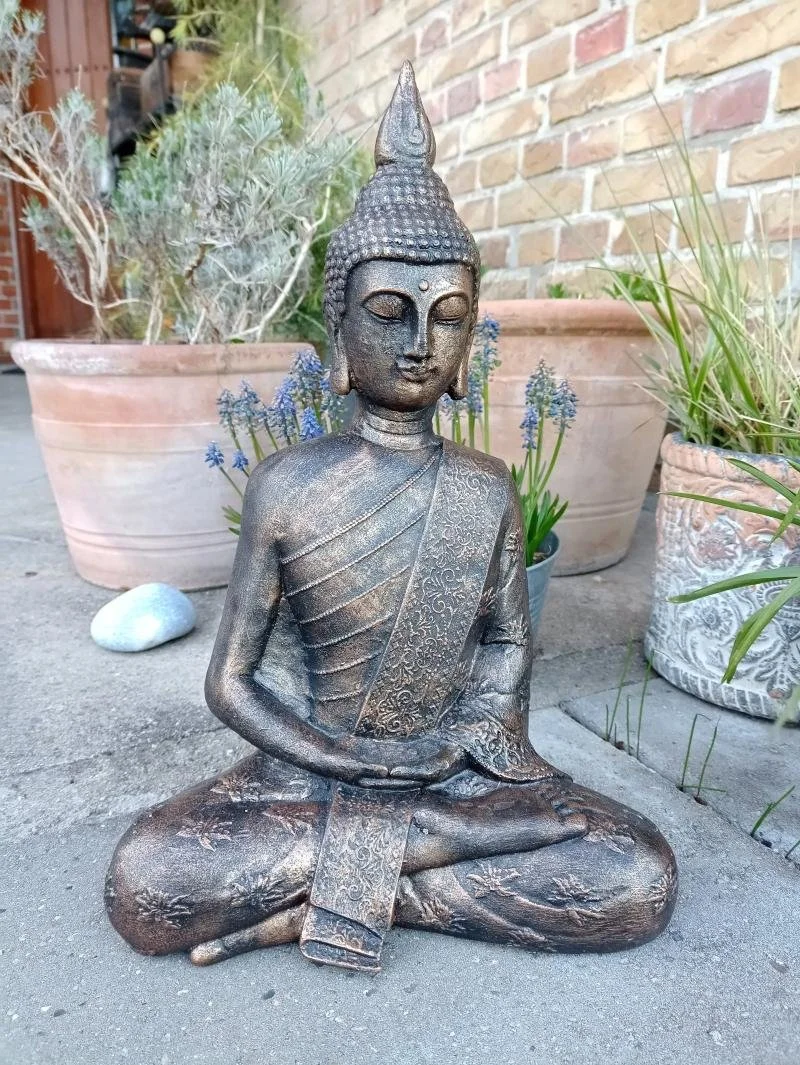 Bronzefarvet Buddha-statue i meditationsstilling omgivet af planter. Et symbol på Ashtanga Yoga.
