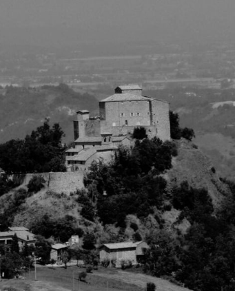 A historic stone castle on a hill overlooking a small town with trees and houses.