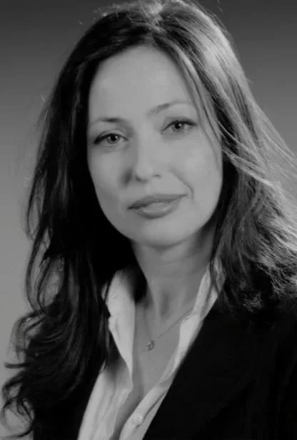 Black and white portrait of a woman with long wavy hair wearing a blazer and a white shirt.