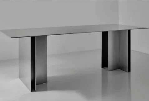 Modern, minimalist gray desk with straight edges and rectangular legs in a plain, light-colored room.