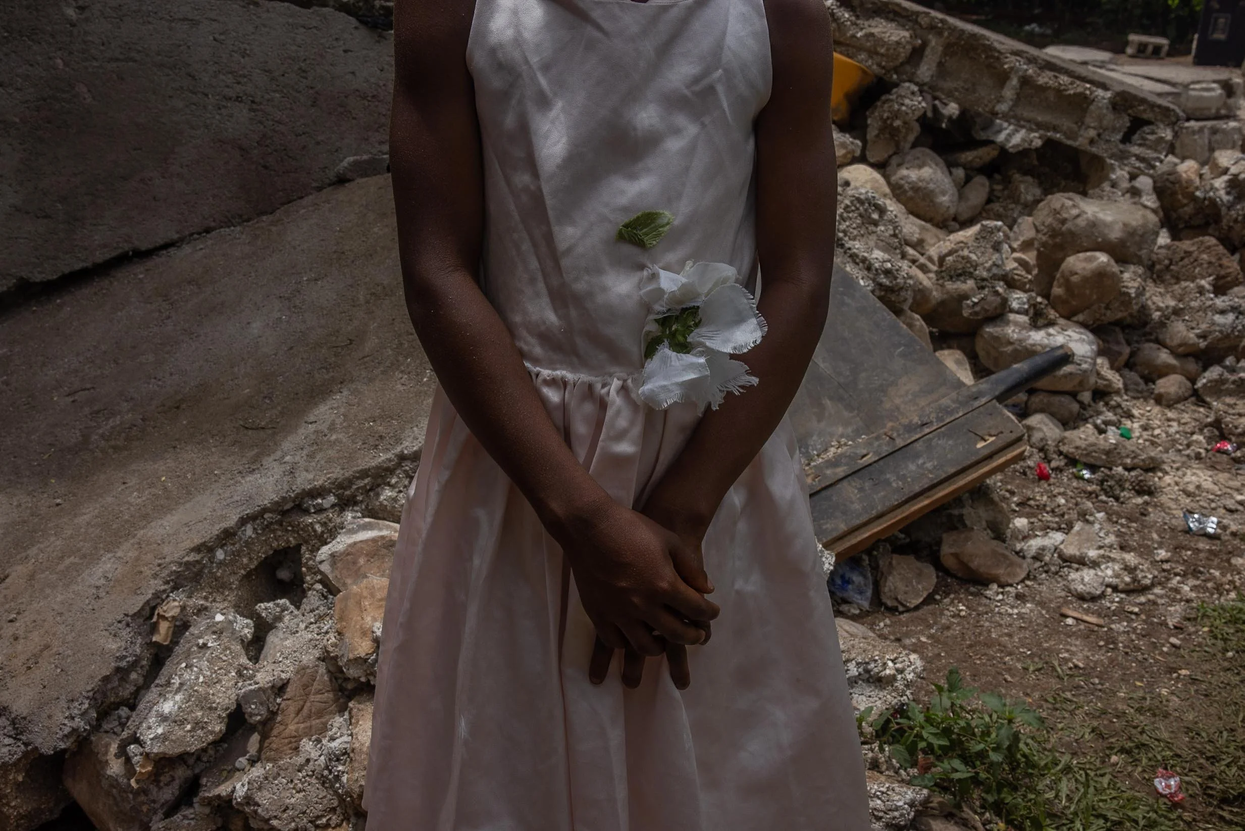 A young girl, dressed for the funeral of Marie Herese Atineus, stands in front of the collapsed home where Marie was killed by falling debris during the August earthquake.  