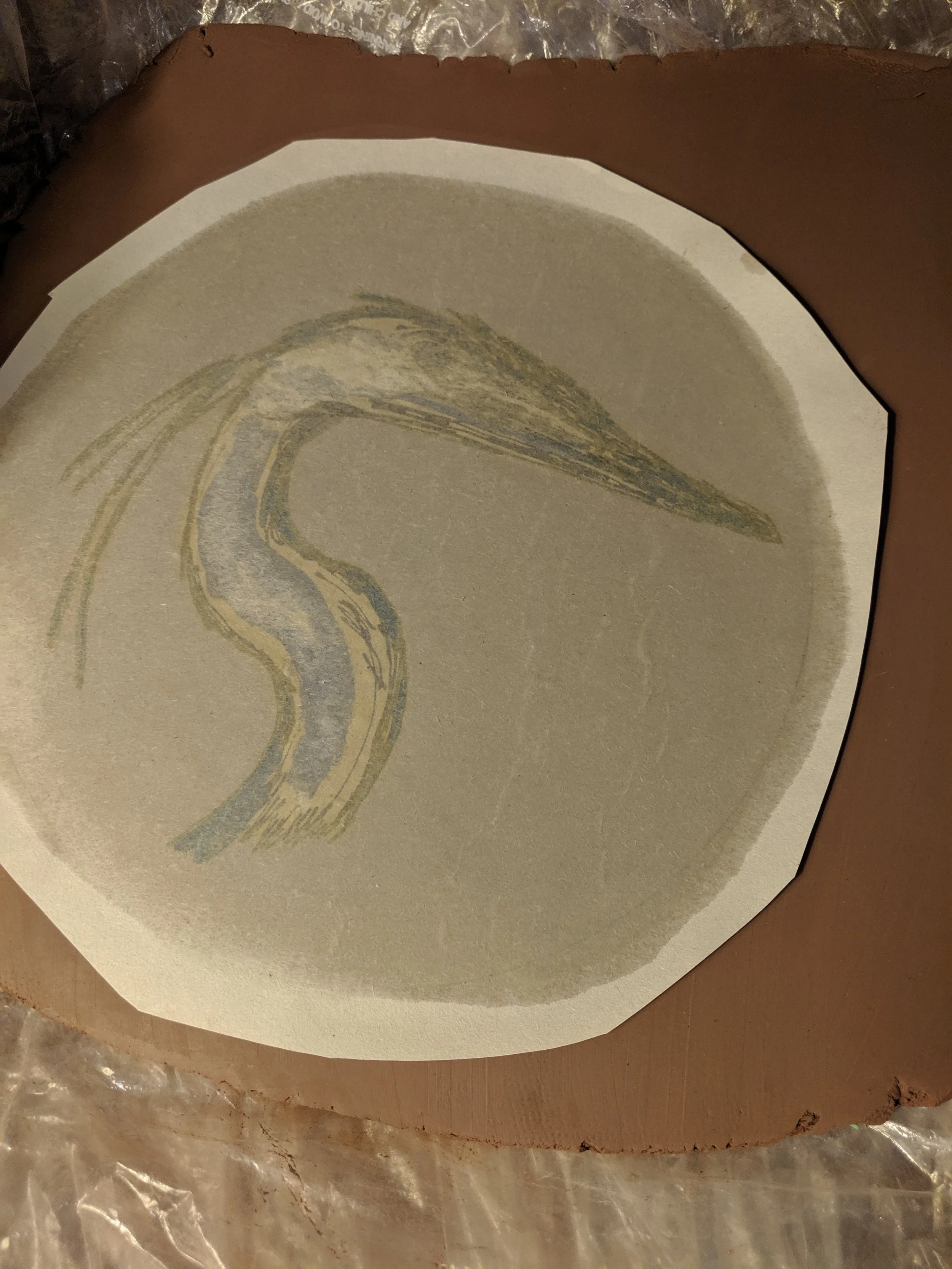 The blue heron underglaze drawing being transferred to the wet clay. This is the back of the newsprint. It will be peeled away soon to leave the bird’s image underneath.