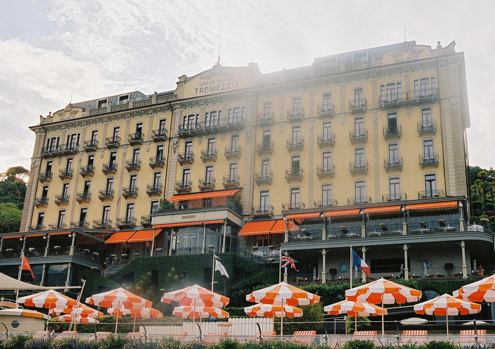 Grand Hotel Tremezzo viewed from the beach with orange and white striped umbrellas at golden hour, Lake Como, Italy, destination wedding photography — The Lopes Photography