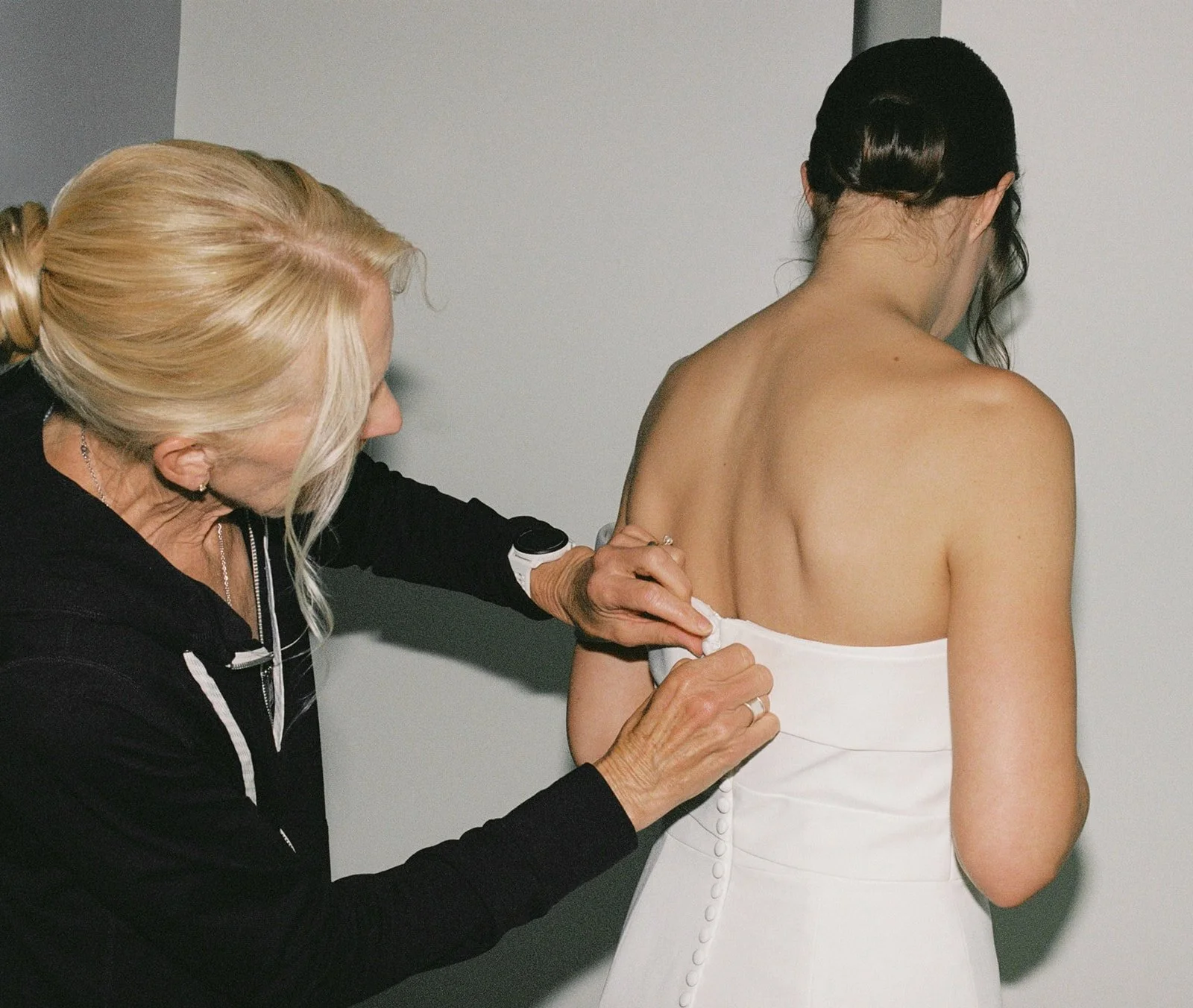 Mother of the bride helping fasten the buttons of a wedding dress during getting ready, photographed in a quiet indoor moment in Portugal