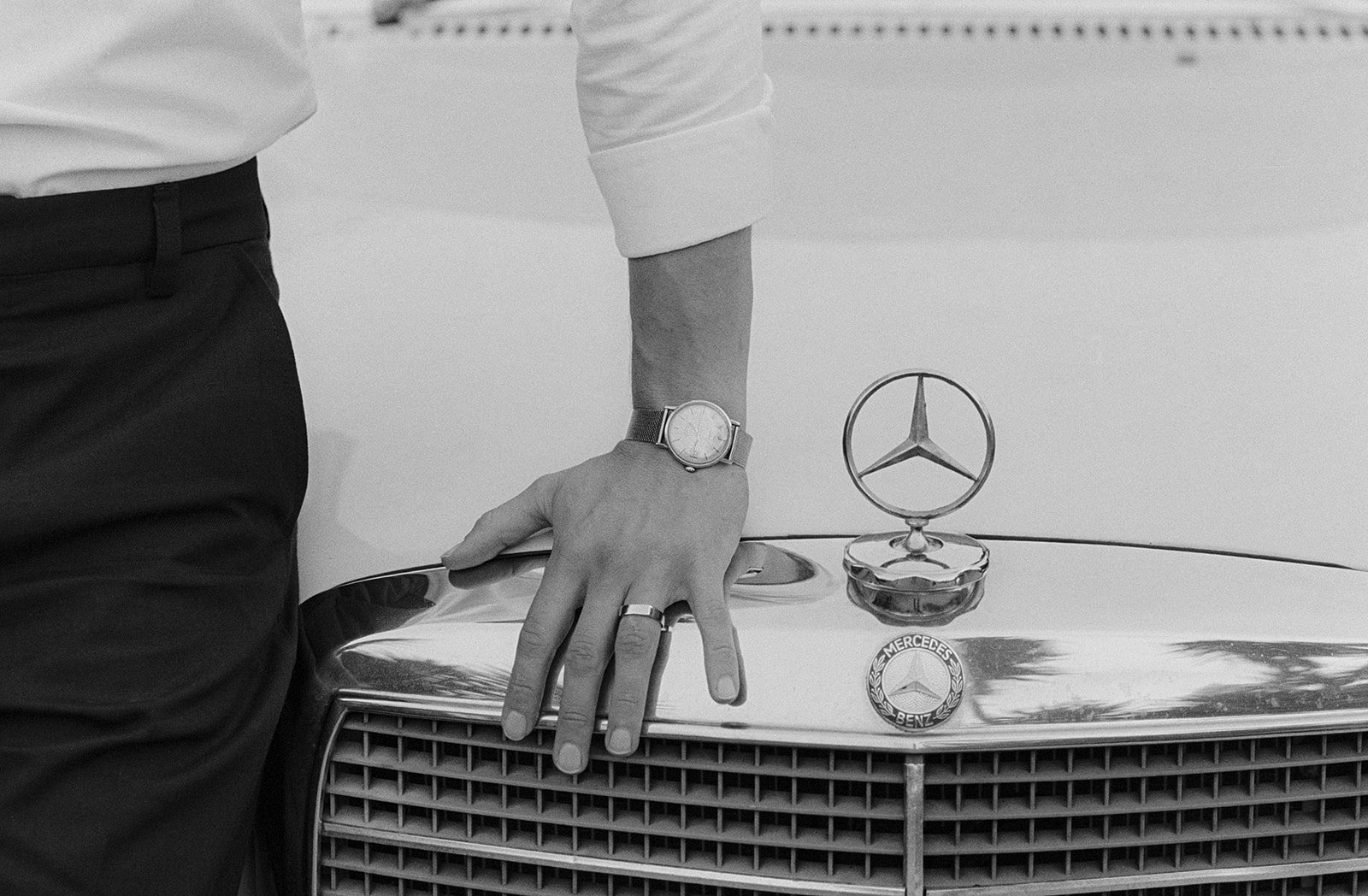 Black and white photo of a groom's hand next to the Merdeces iconic symbol in a classic car