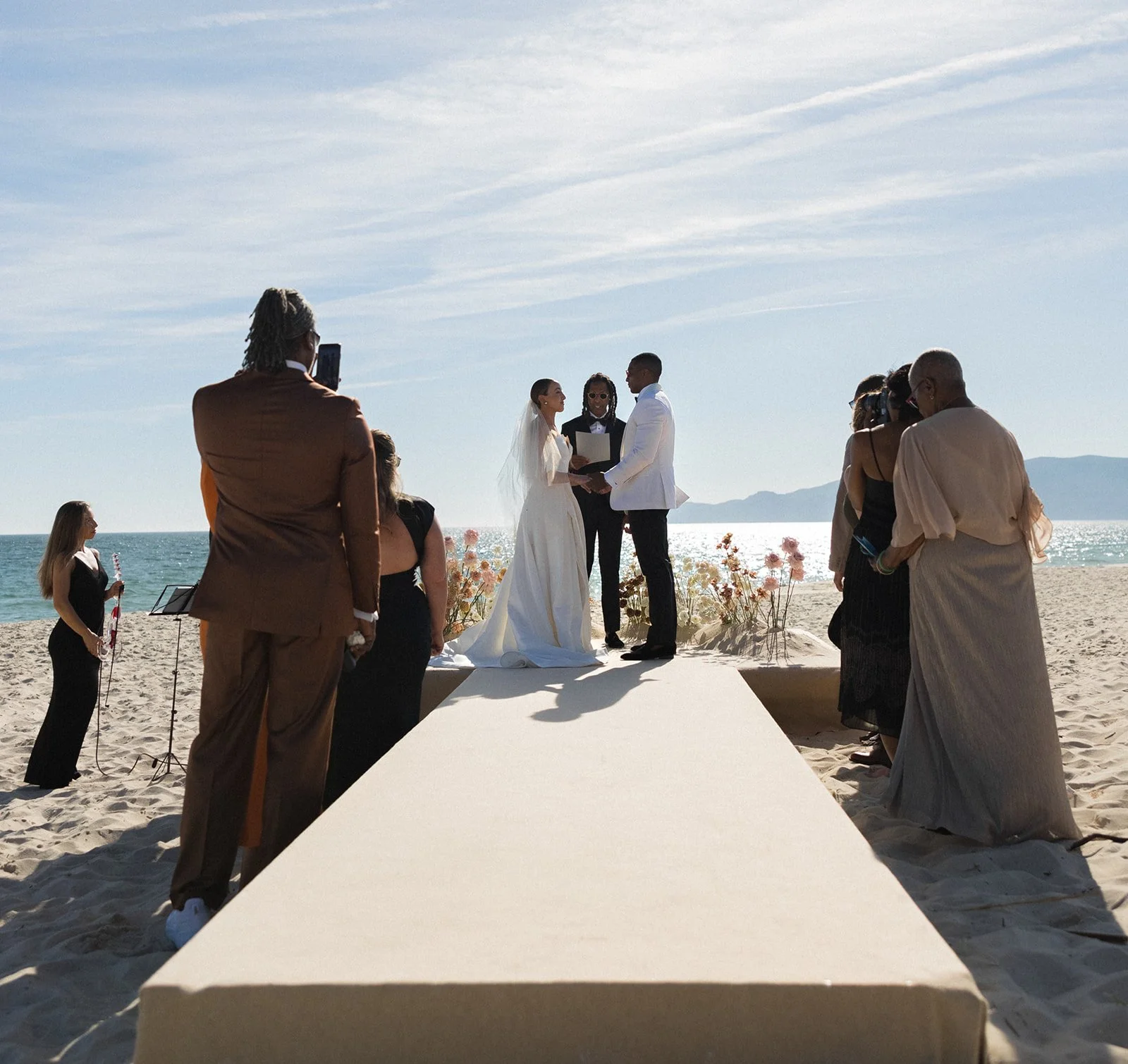 Beach wedding ceremony, bride and groom at the altar with ocean and mountains under clear blue sky | The Lopes Photography