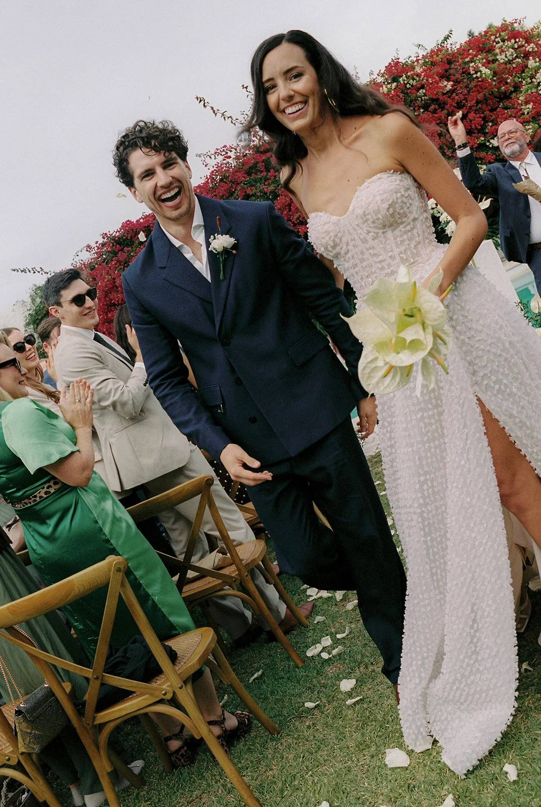 Newlyweds walking down the aisle at Marqí, smiling among their guests as flower petals scatter across the ground — wedding photography by The Lopes Photography