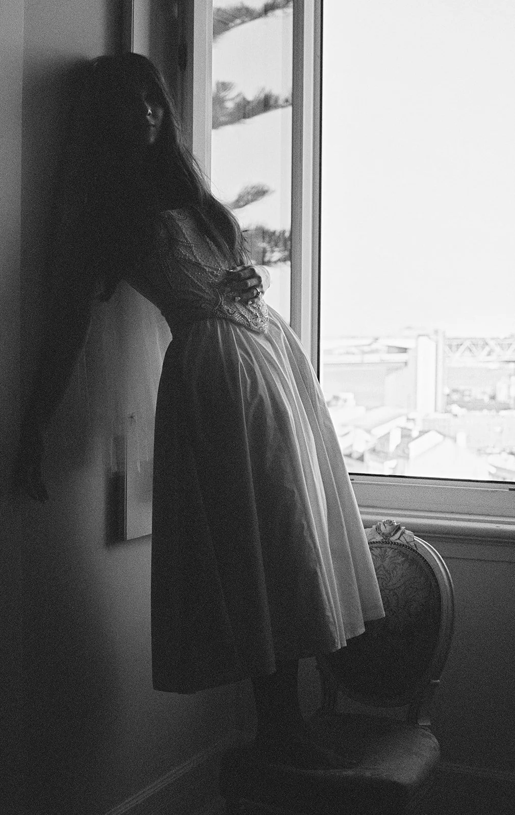 Bride in silhouette at a tall window inside Pestana Palace Lisbon, with the Lisbon skyline and the 25 de Abril Bridge framed in the background