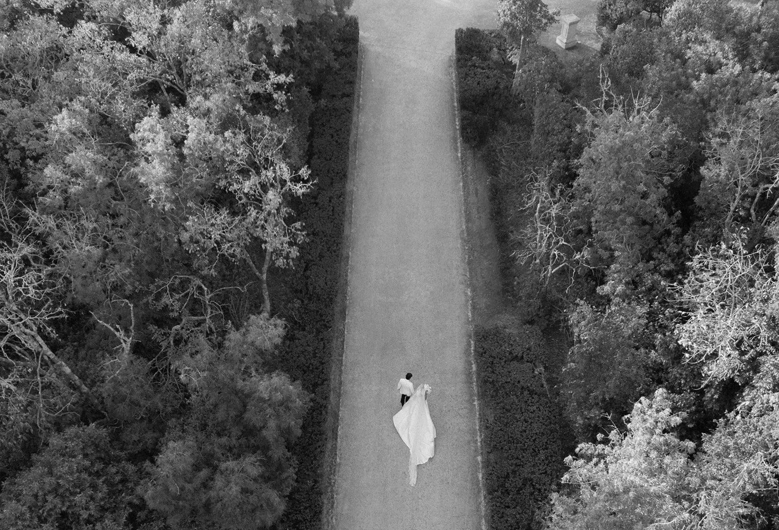 Black and white aerial view of newlyweds walking alone down a long tree-lined path at Palácio de Queluz, intimate and spontaneous — Vogue Arabia wedding photography Portugal
