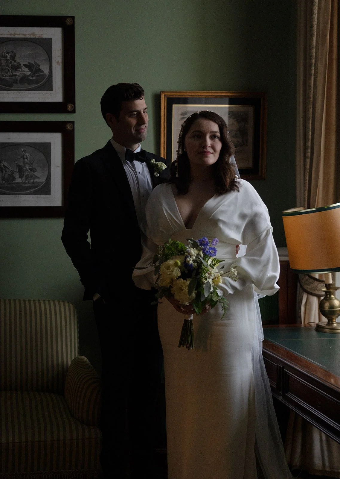 Bride and groom in the green-walled study room at Grémio Literário in Lisbon, surrounded by framed engravings and a warm chandelier, photographed by The Lopes Photography