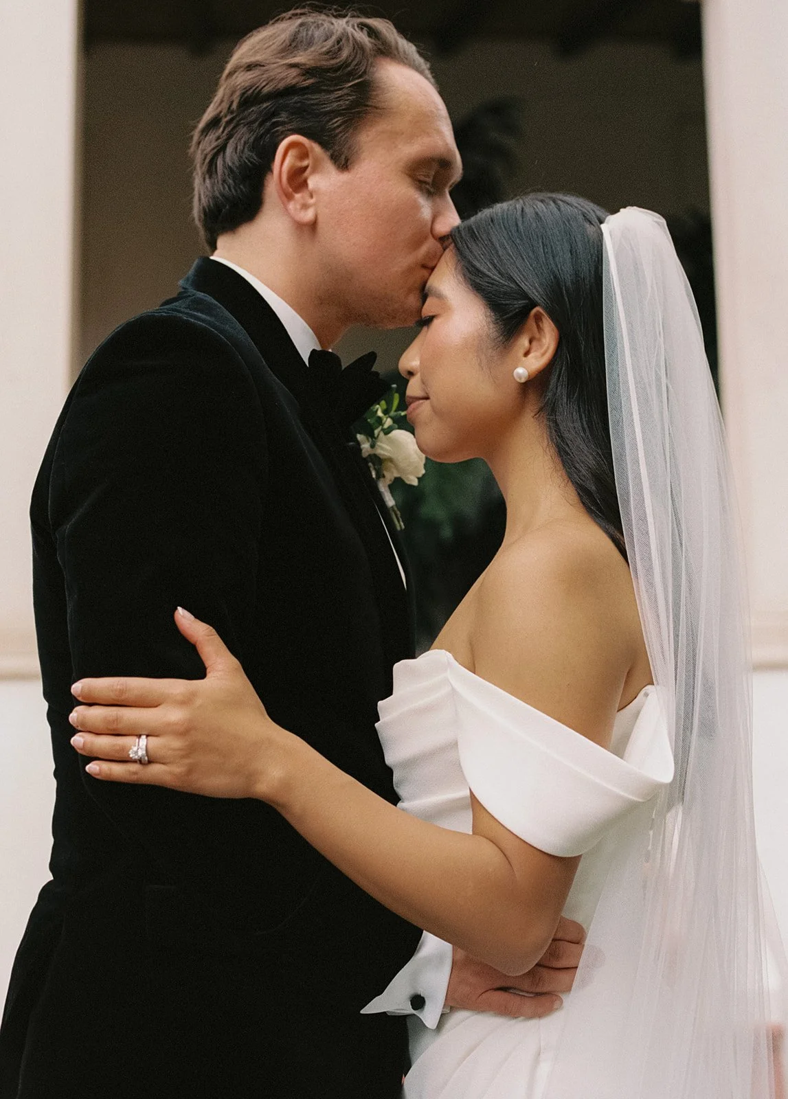 Bride and groom facing each other while hugging and the groom is kissing the brides forehead