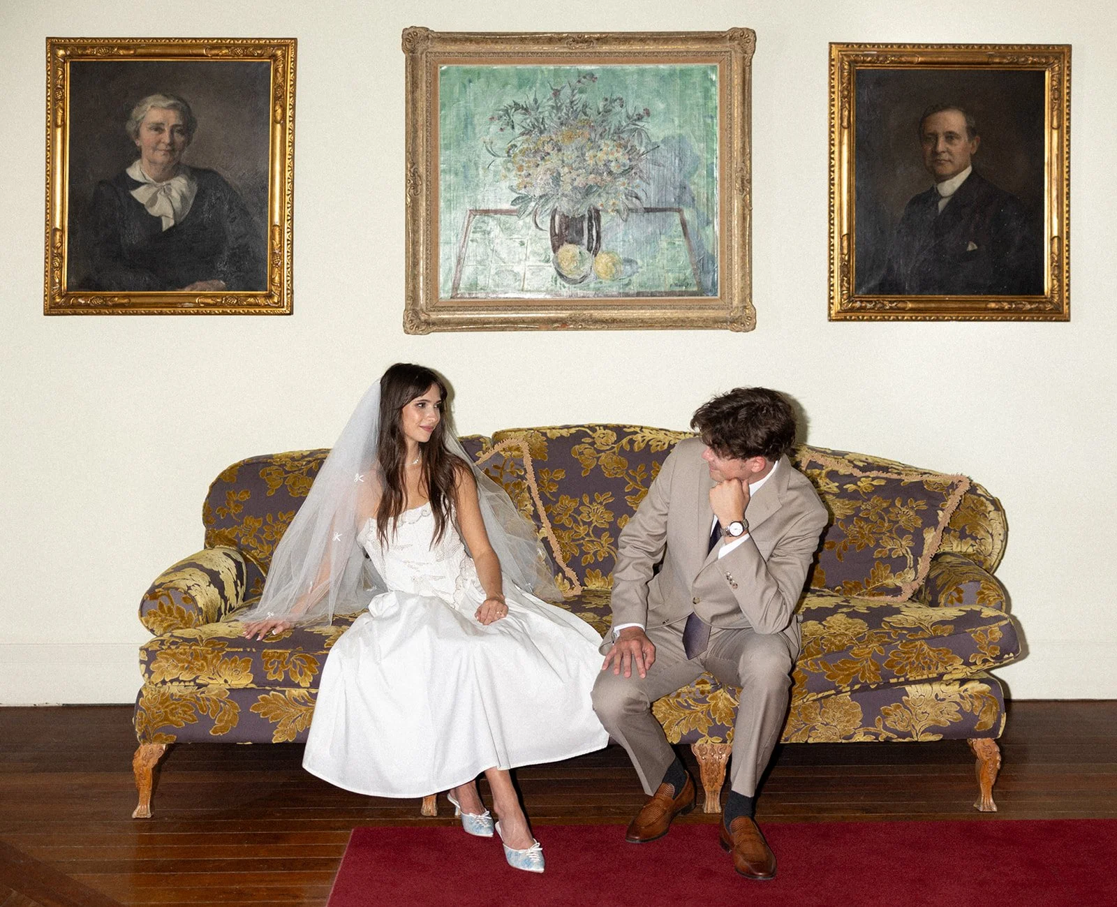 Bride and groom on antique sofa beneath portrait paintings, luxury wedding venues algarve by The Lopes Photography