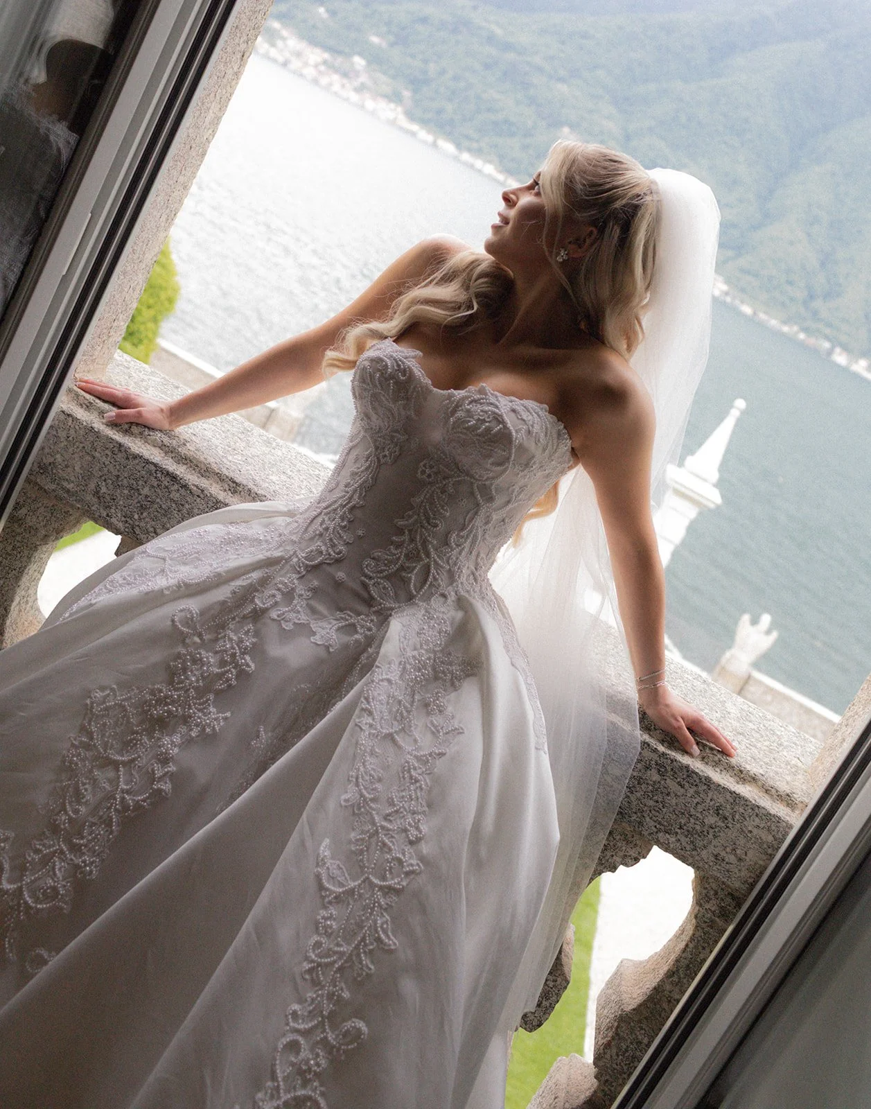 Bride gazing through a stone archway window at Villa Balbiano overlooking Lake Como, Italy, destination wedding photography — The Lopes Photography