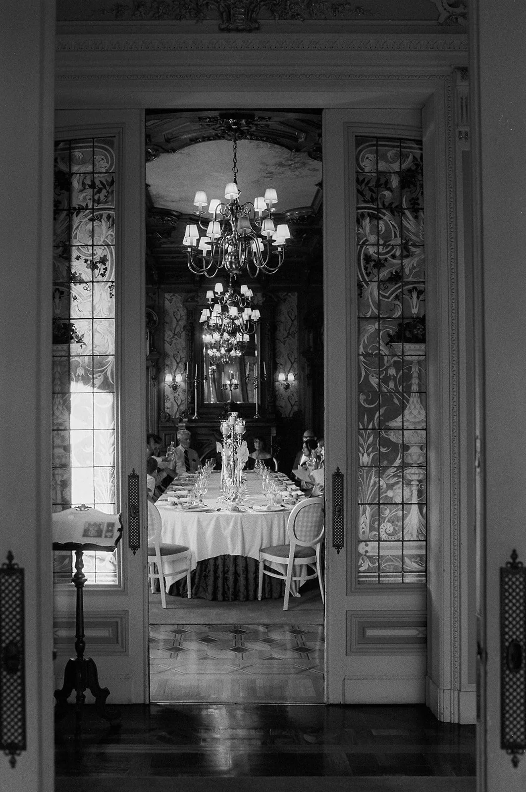 Black and white view through ornate palace doors into the candlelit wedding reception at Pestana Palace Lisbon, destination wedding photography Portugal | The Lopes Photography