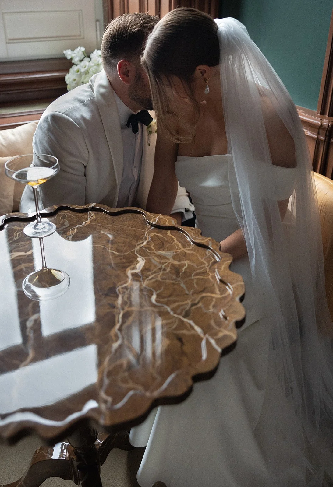 Couple leaning together at a marble-top table with a coupe cocktail glass, La Distillerie wedding in Lisbon | The Lopes Photography