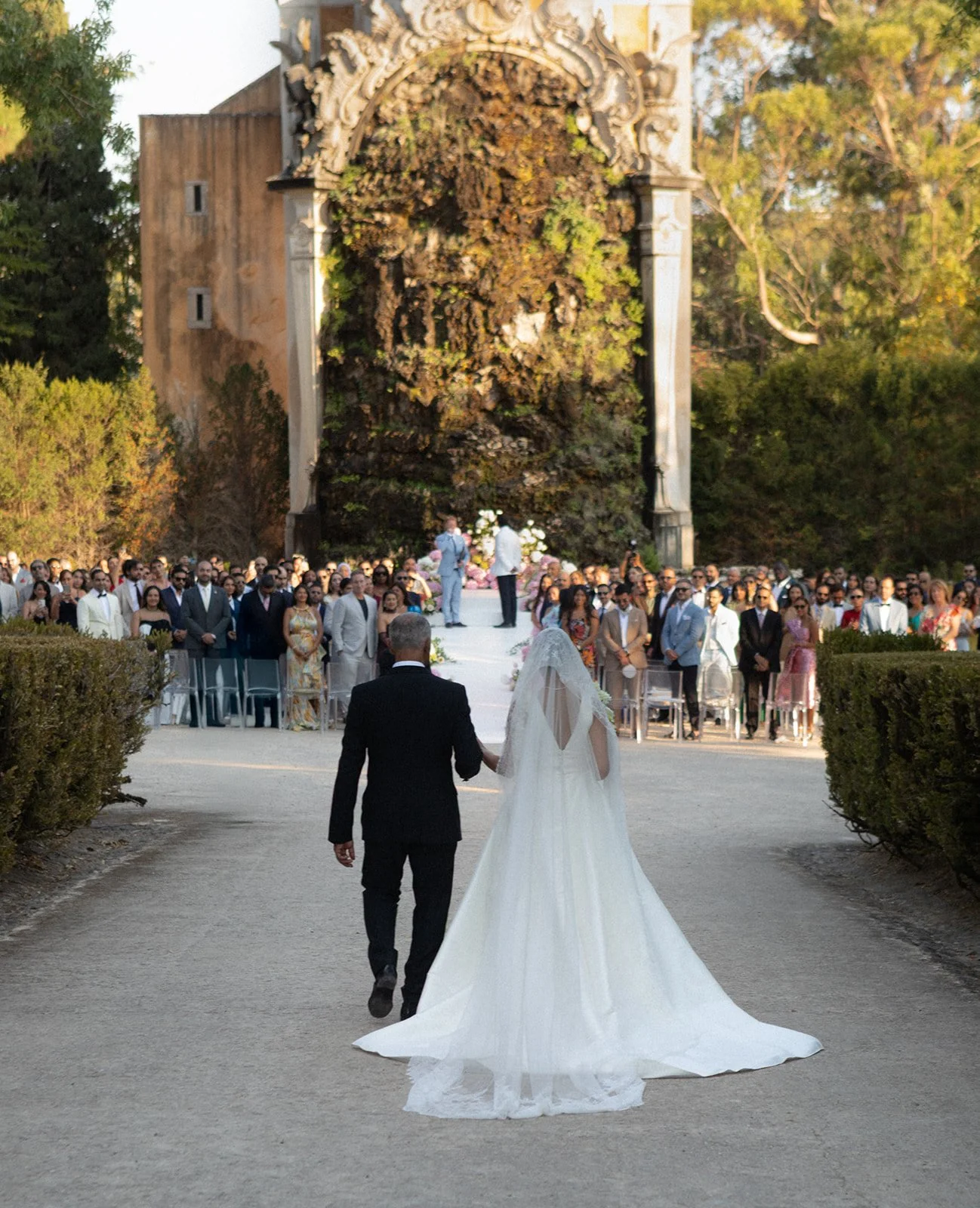 Father of the bride walking down the bride a the ceremony aisle in the formal gardens of a palace in Portugal at golden hour.